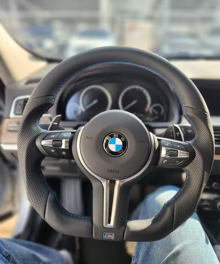 BMW steering wheel with blue stitching, mounted on a car dashboard.