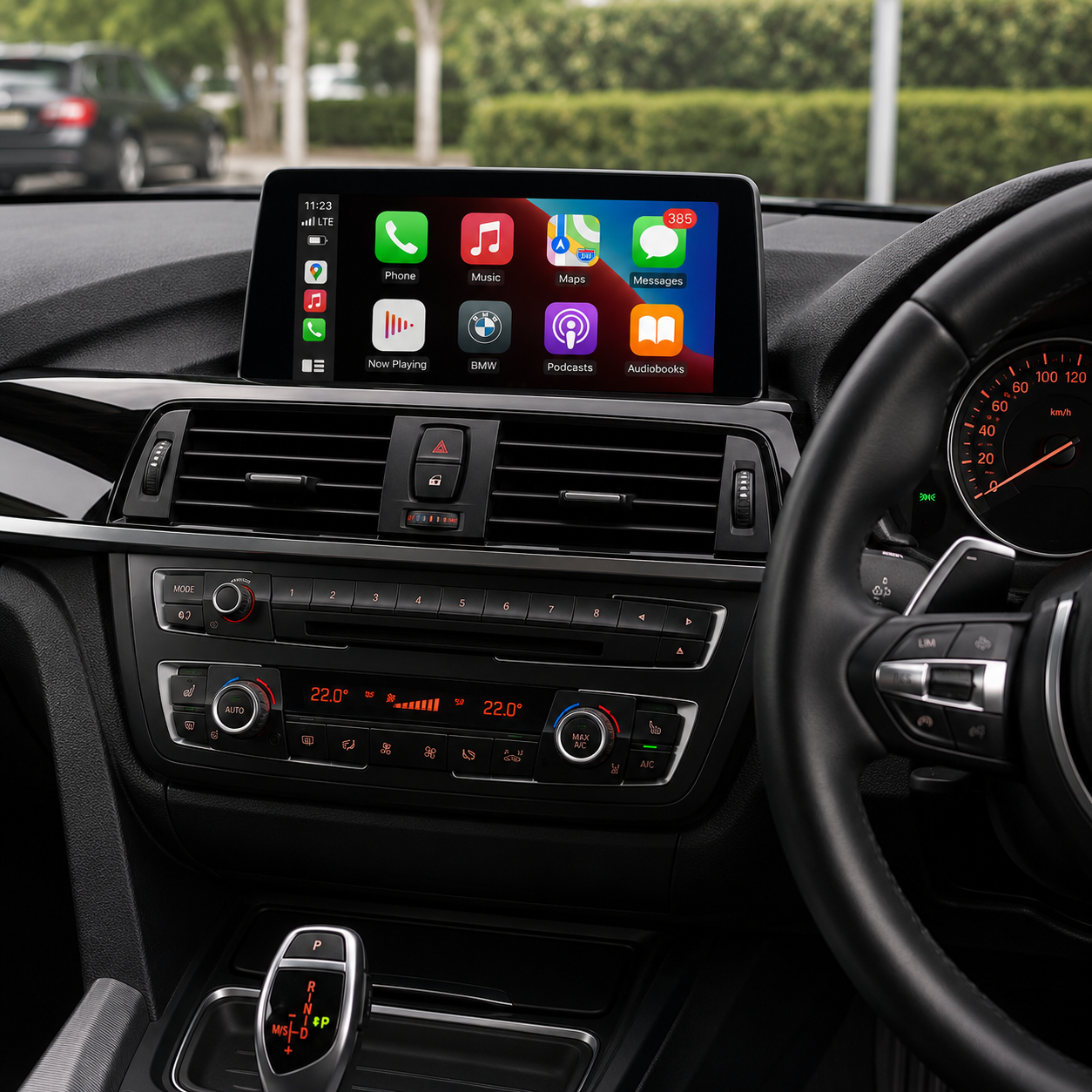 The interior of a car dashboard displaying a digital infotainment screen showing apps like Phone, Music, Maps, Messages, Podcasts, and Audiobooks. The car has climate controls set to 22°C and a gear shift in park.