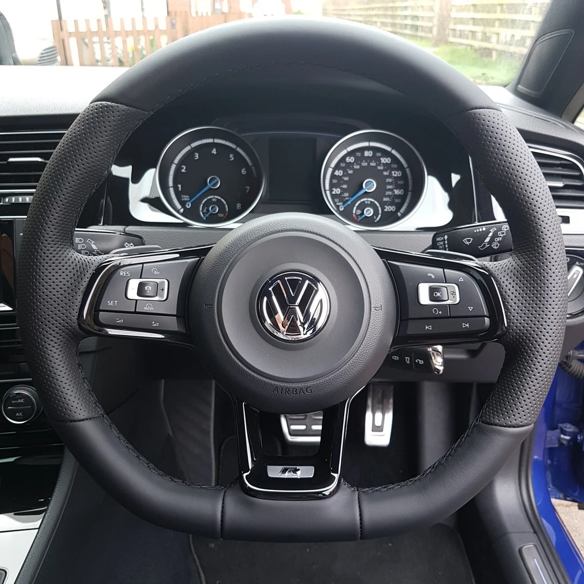 Inside view of a Volkswagen car dashboard and steering wheel, featuring speedometers, control buttons, and a Volkswagen emblem in the center of the steering wheel.
