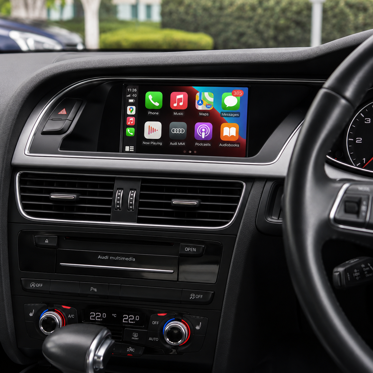Close-up of a car's dashboard with a digital infotainment screen displaying Apple CarPlay apps, including Phone, Music, Maps, Messages, Now Playing, Audi MMI, Podcasts, and Audiobooks. The dashboard shows air vents, climate controls, and part of the steering wheel.