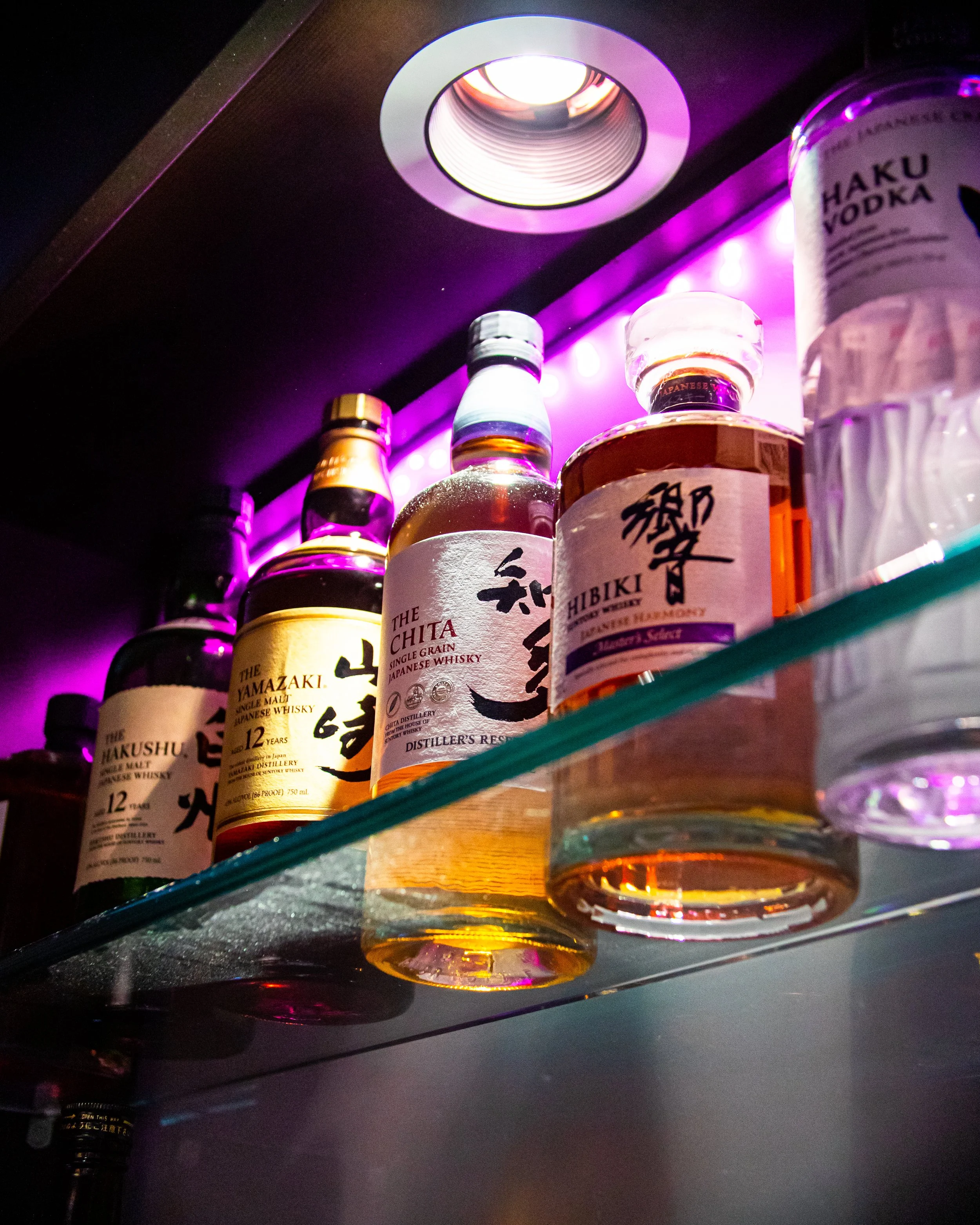 Bottles of Japanese whiskey displayed on a shelf with purple lighting above.