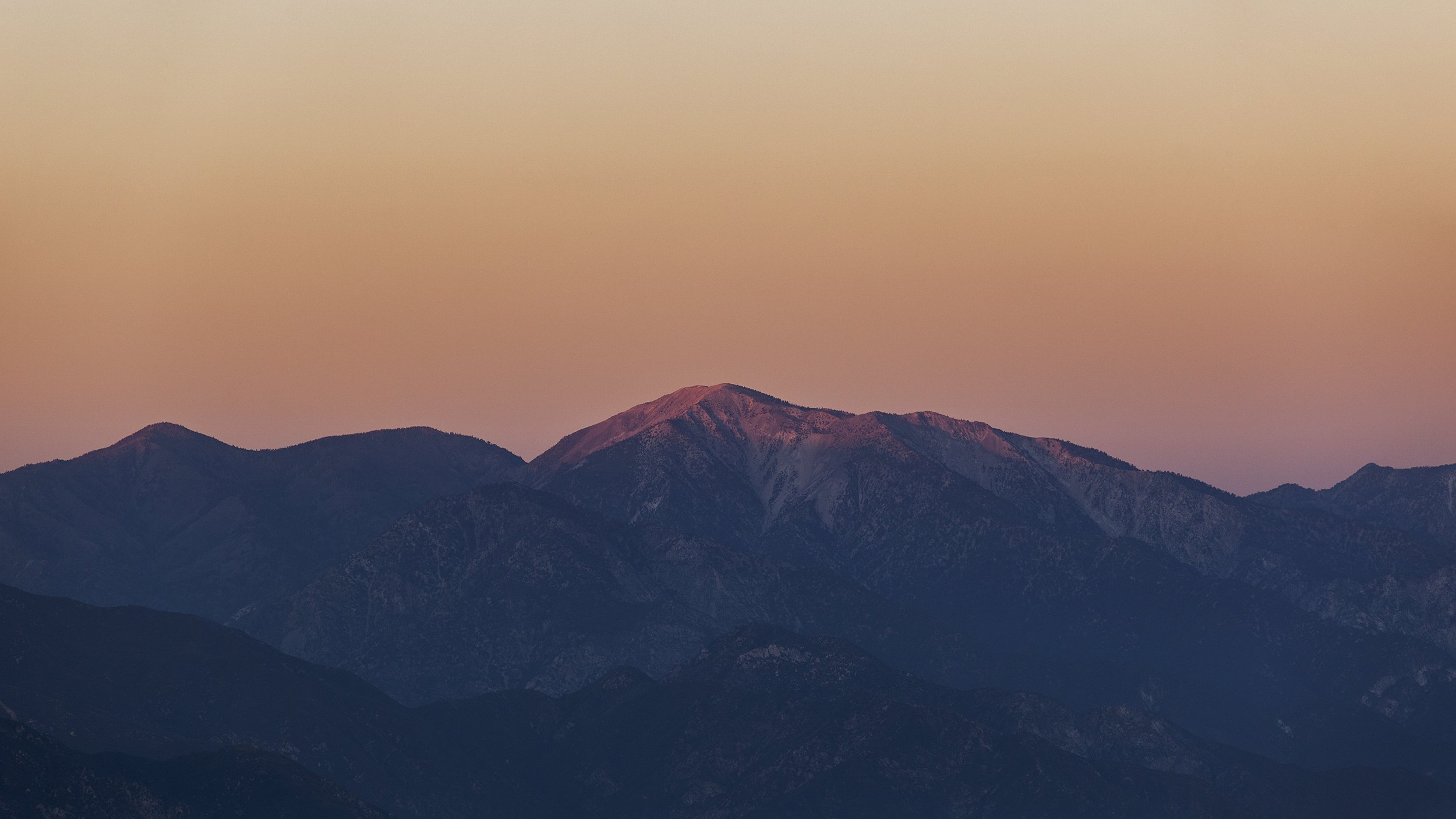 A mountain range at sunset with a pinkish sky and shadows on the mountains.