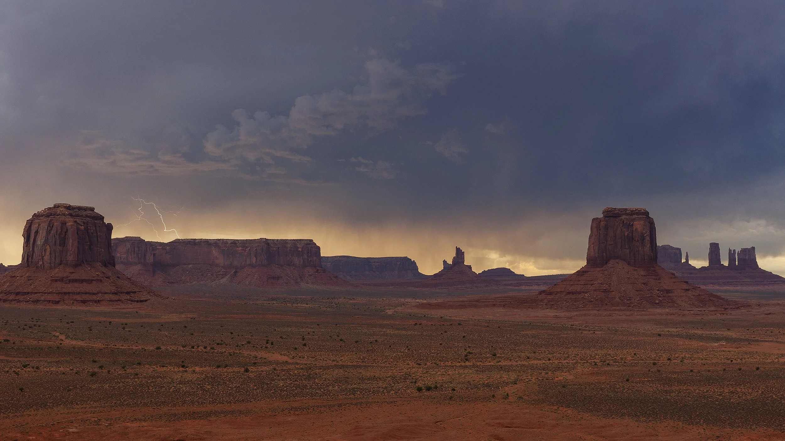 A desert landscape with large sandstone formations under a dark, stormy sky with lightning.