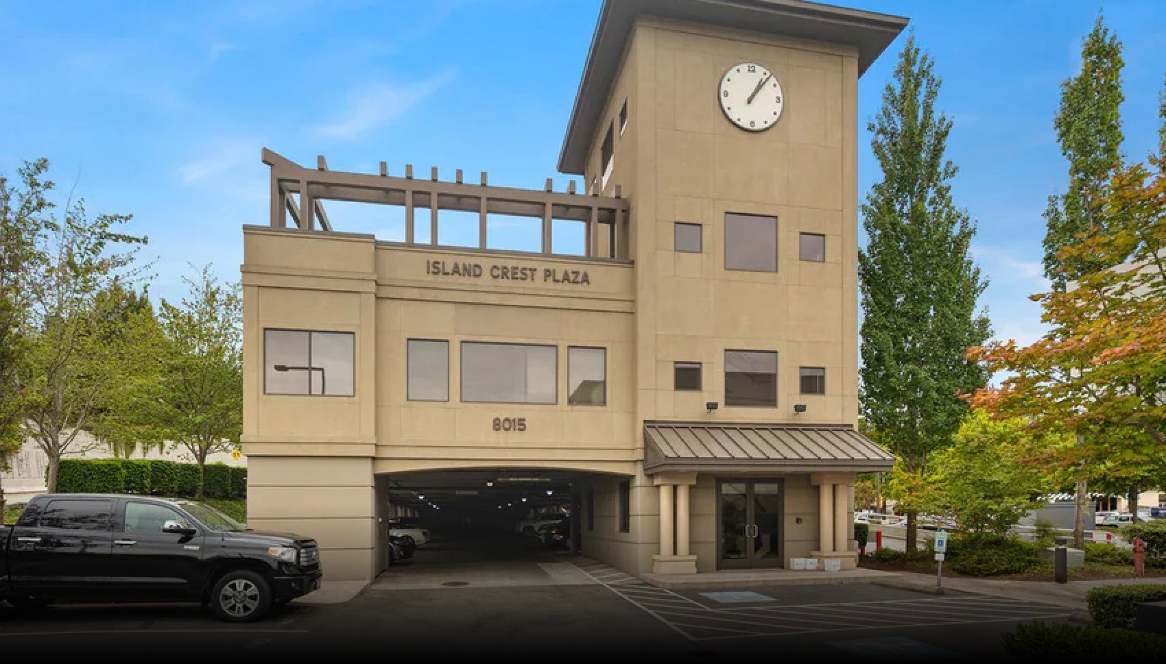 Building with a sign reading 'Island Crest Plaza' and the number '8015', featuring a parking garage entrance and surrounded by trees.
