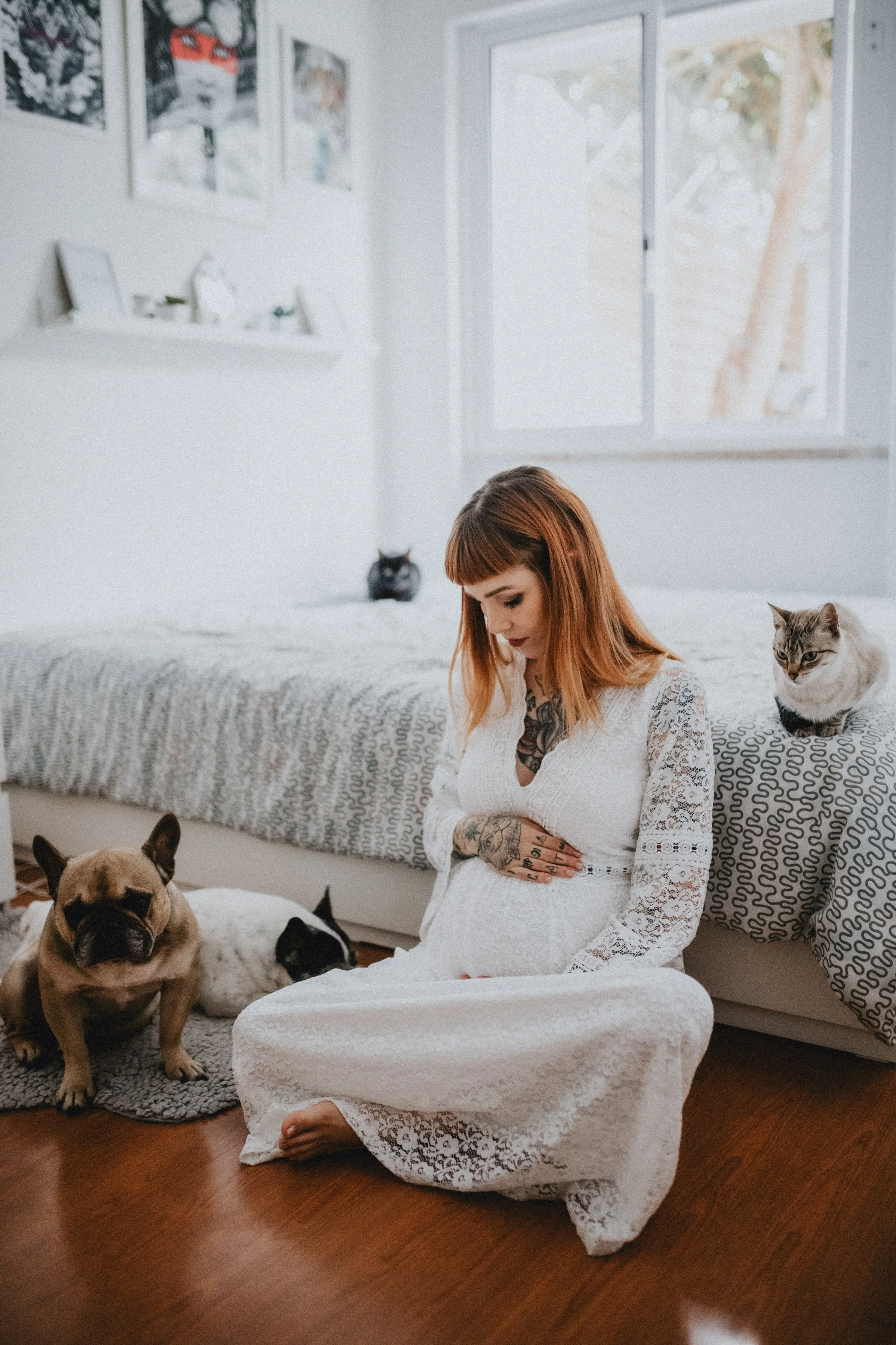 Intimate maternity photoshoot at home featuring pregnant woman in white dress sitting on the floor with her dogs in Portugal.