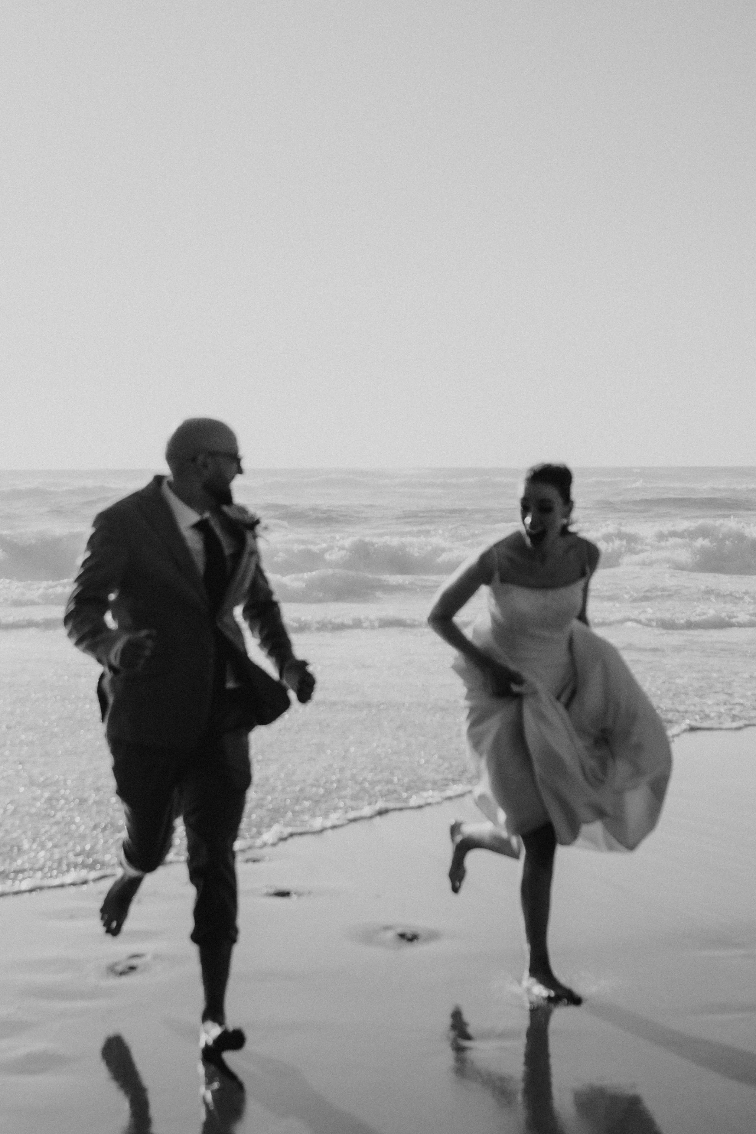 Black and white photo of couple walking barefoot during coastal elopement in Portugal