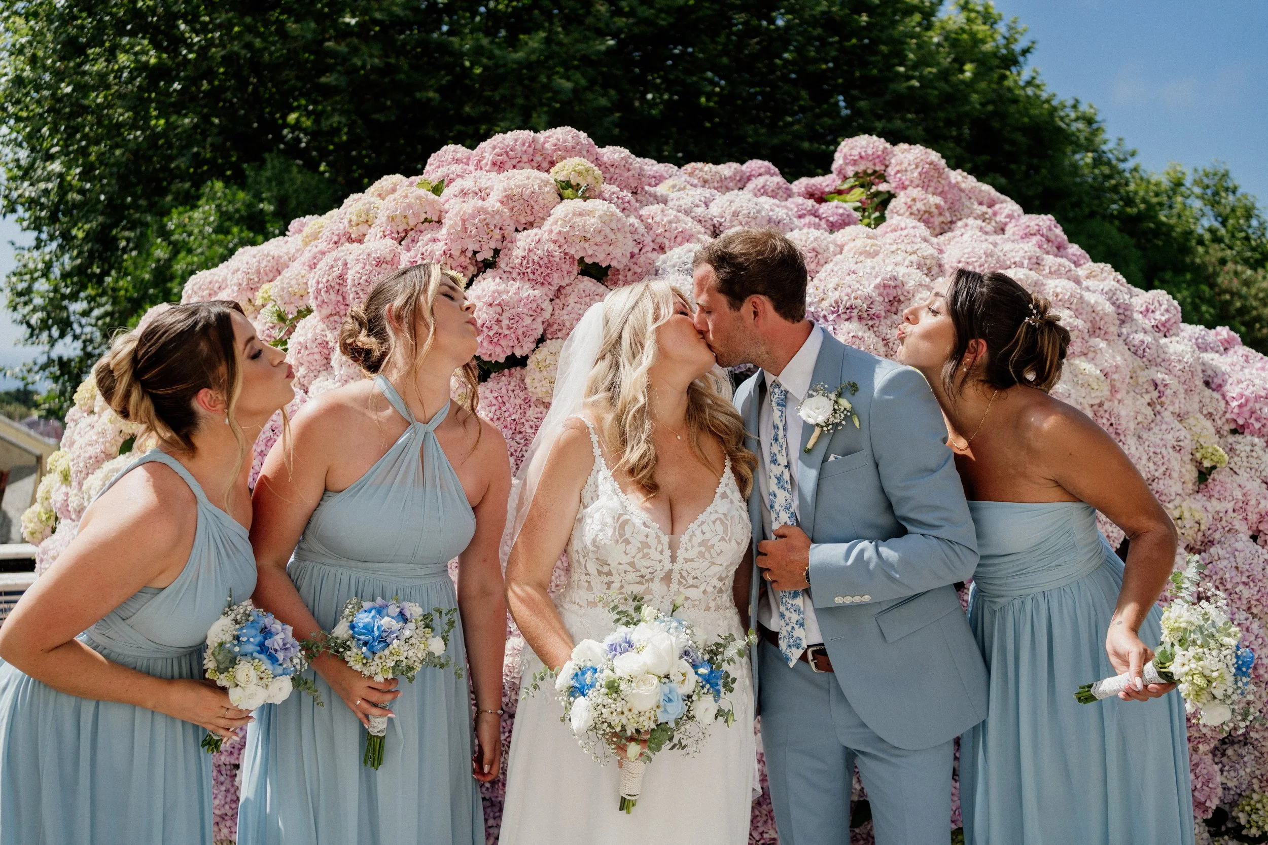 Bridal party celebrating under pink floral arch during romantic outdoor wedding in Portuga