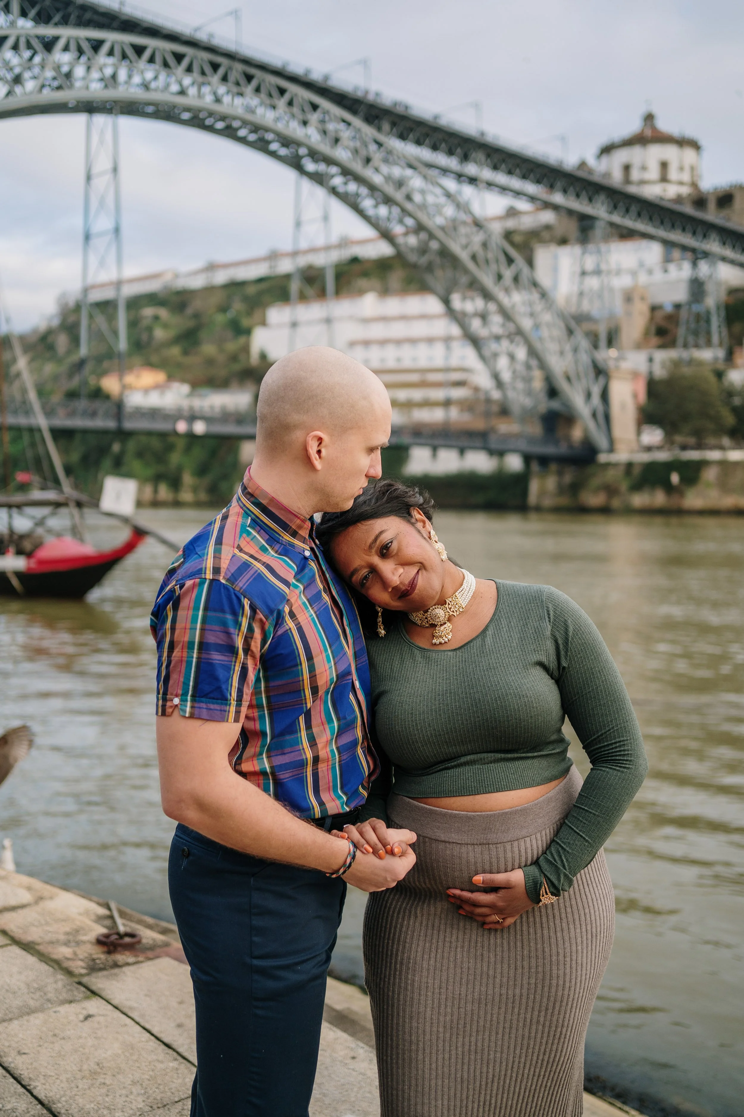 Maternity photoshoot in Porto featuring couple embracing near Dom Luís I Bridge during pregnancy session