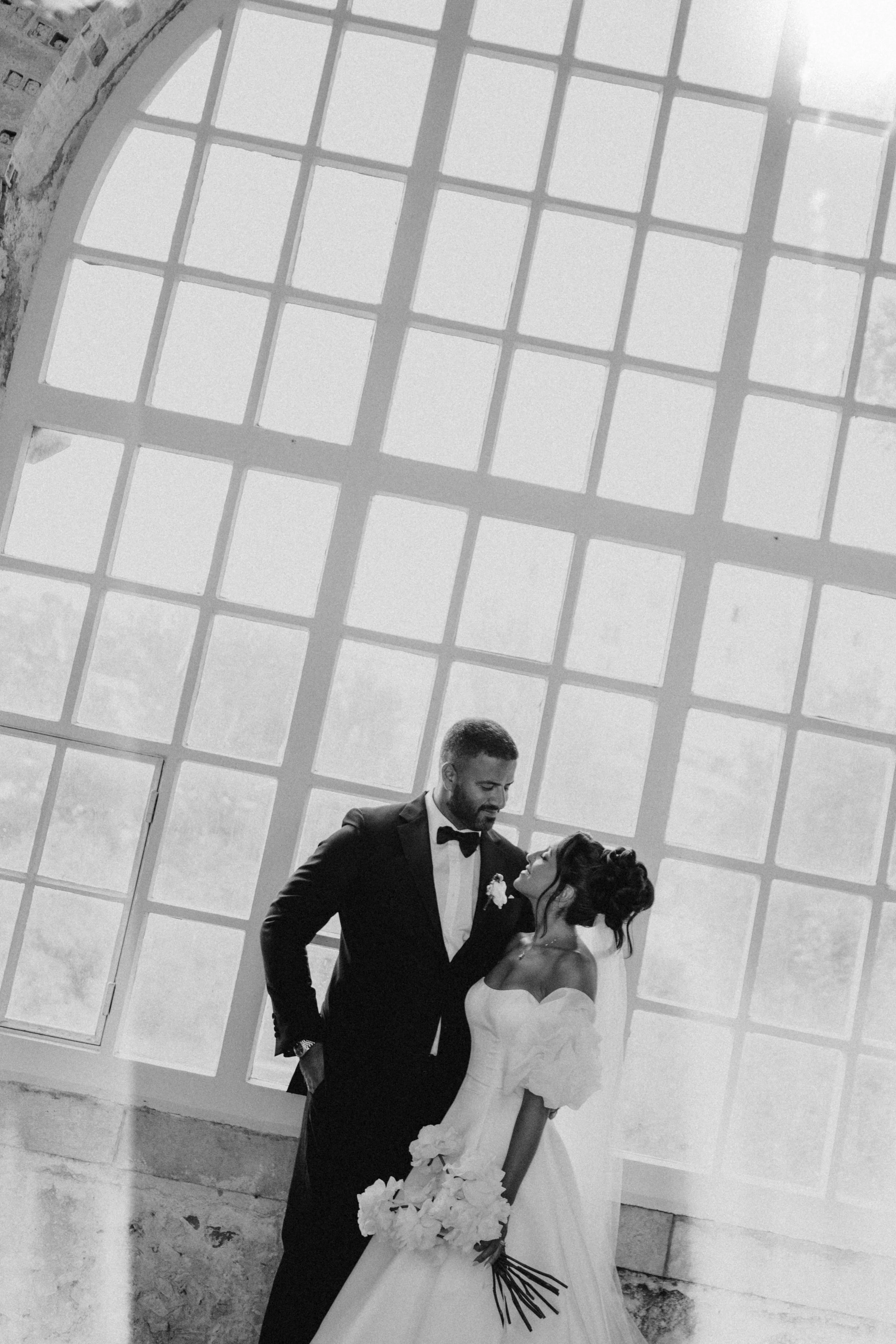 Dramatic black and white wedding portrait of couple silhouetted against large window