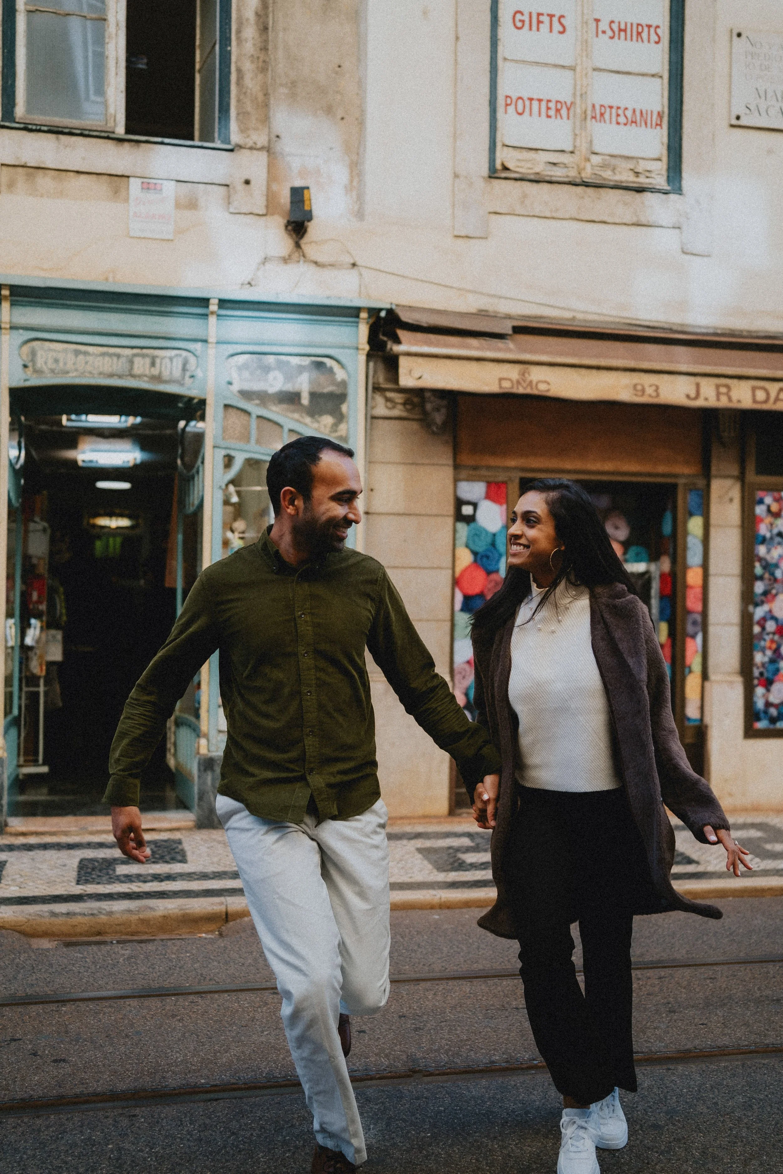 Engagement photography in Lisbon, couple walking through historic city street with traditional architecture.
