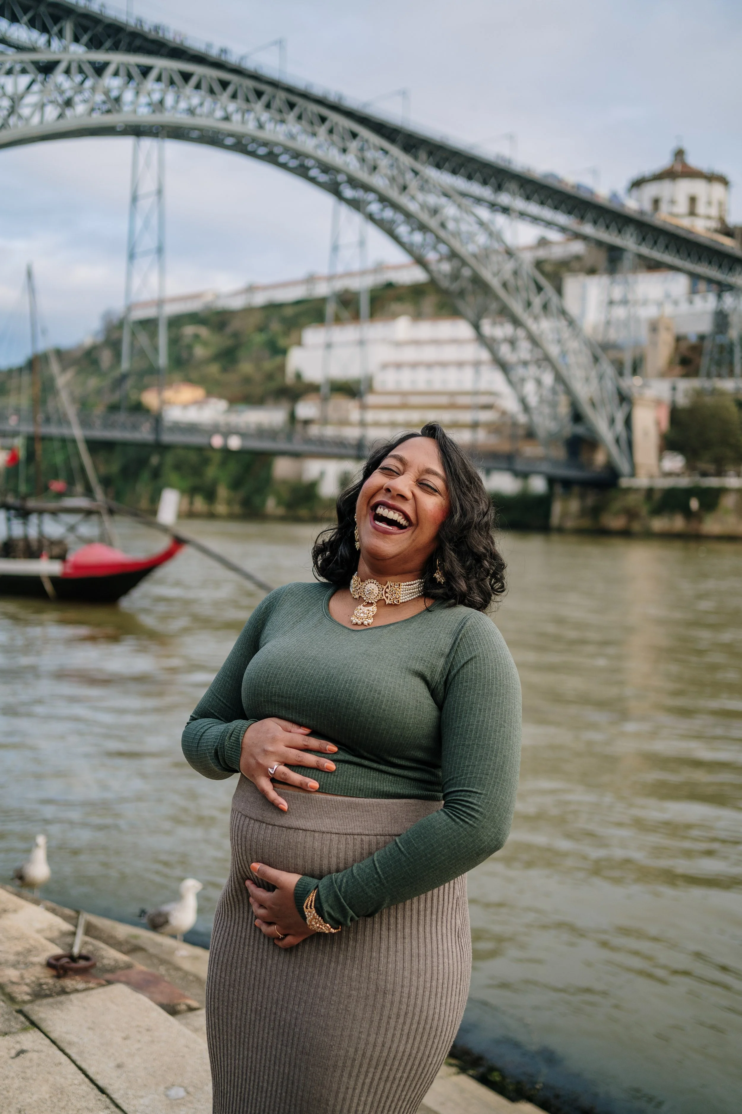 Maternity photoshoot in Porto featuring couple embracing near Dom Luís I Bridge during pregnancy session