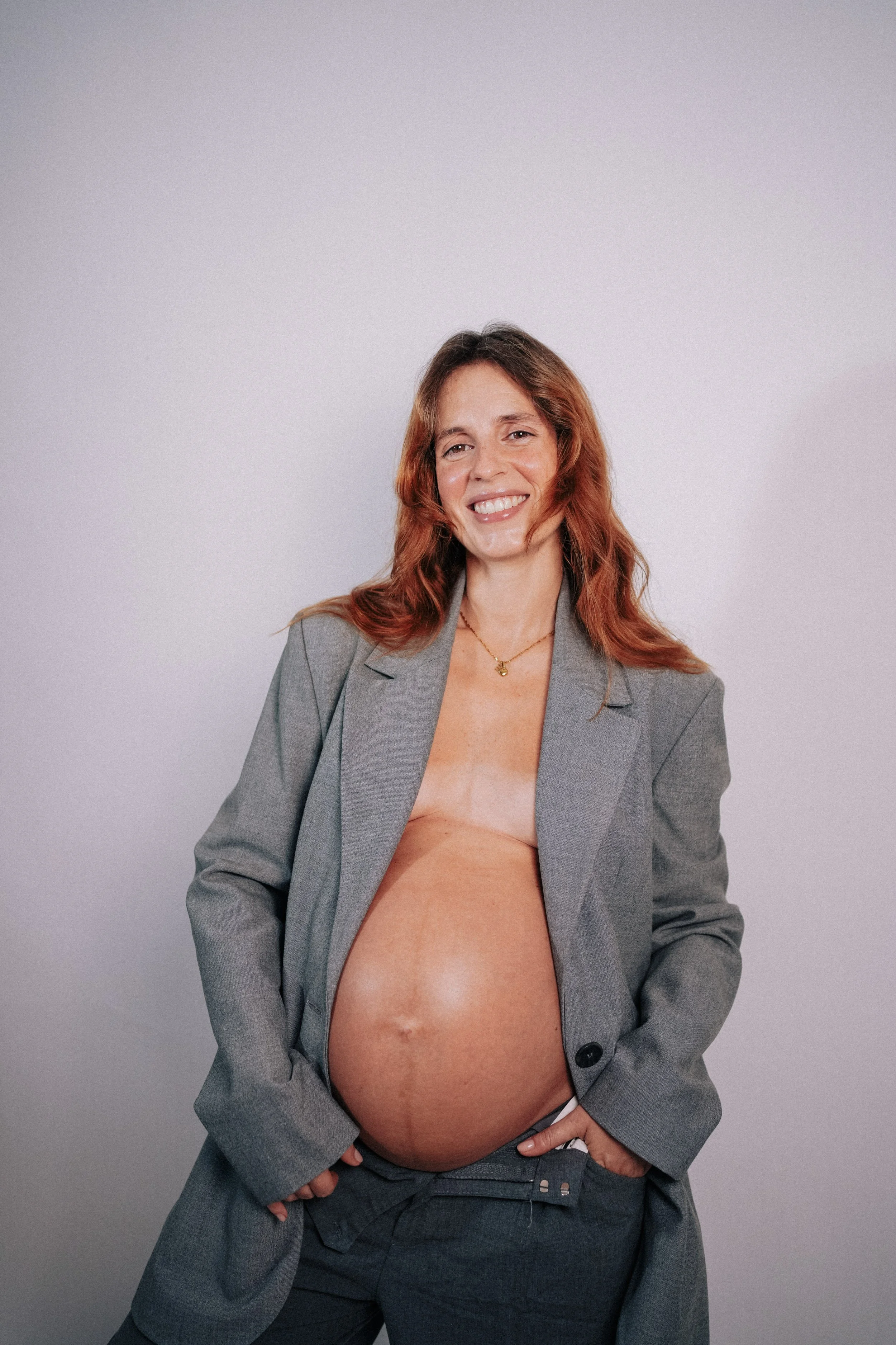 Elegant studio maternity portrait of pregnant woman wearing grey blazer in Portugal.