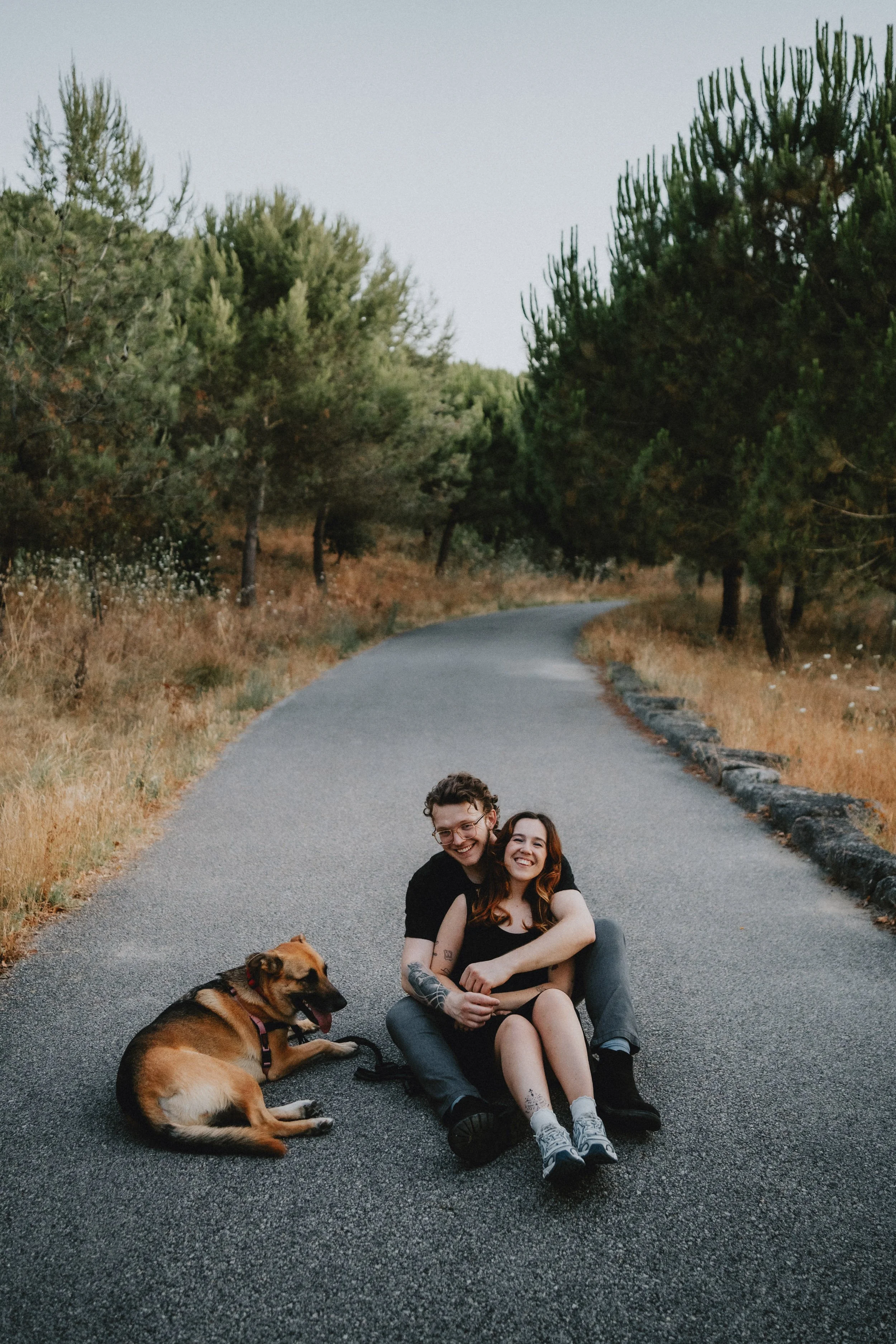 Engagement photography in Portugal, couple sitting together on quiet road with their dog during outdoor session.