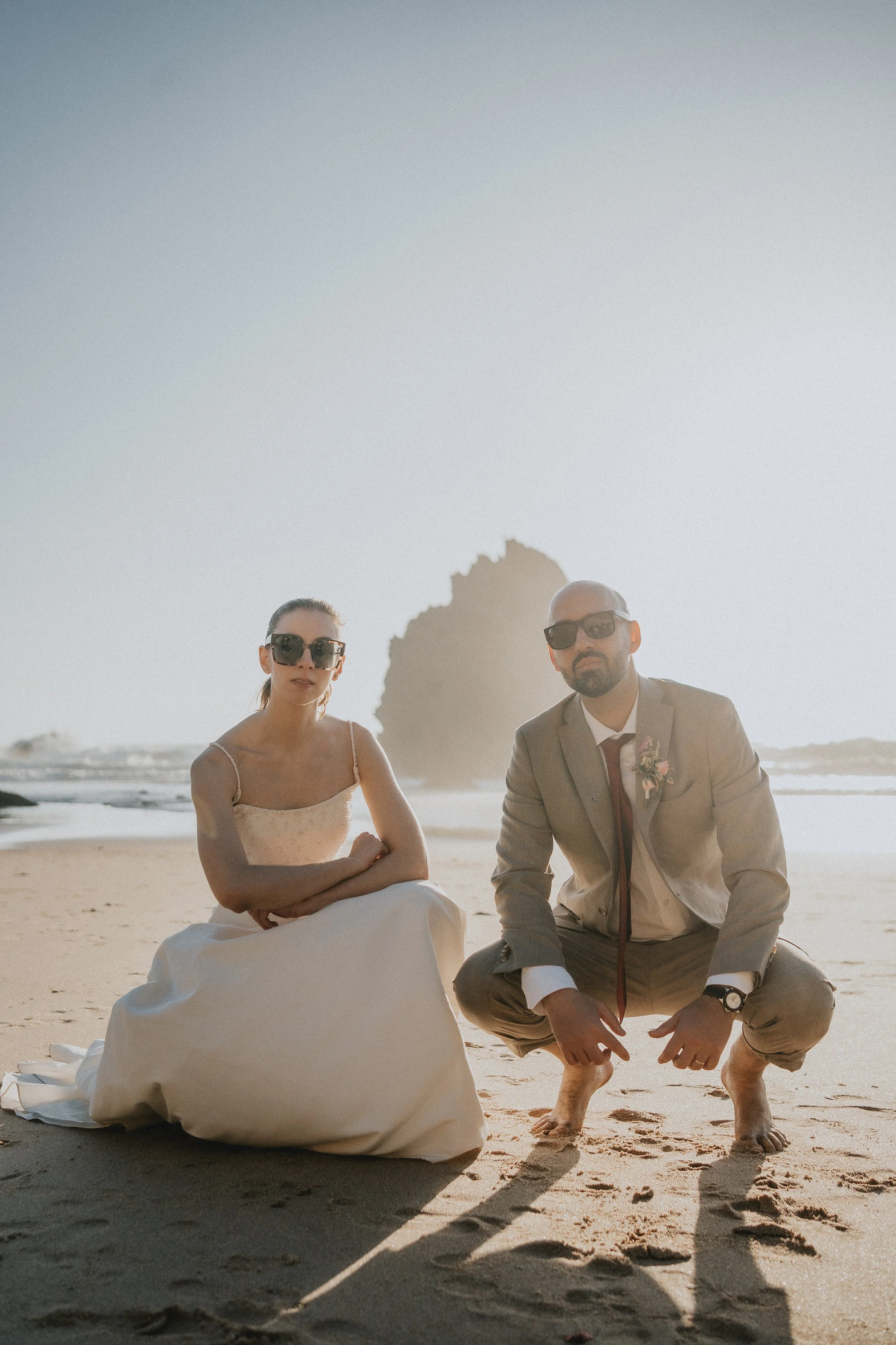 Bride and groom sitting on the sand during an intimate beach elopement in Portugal at sunset