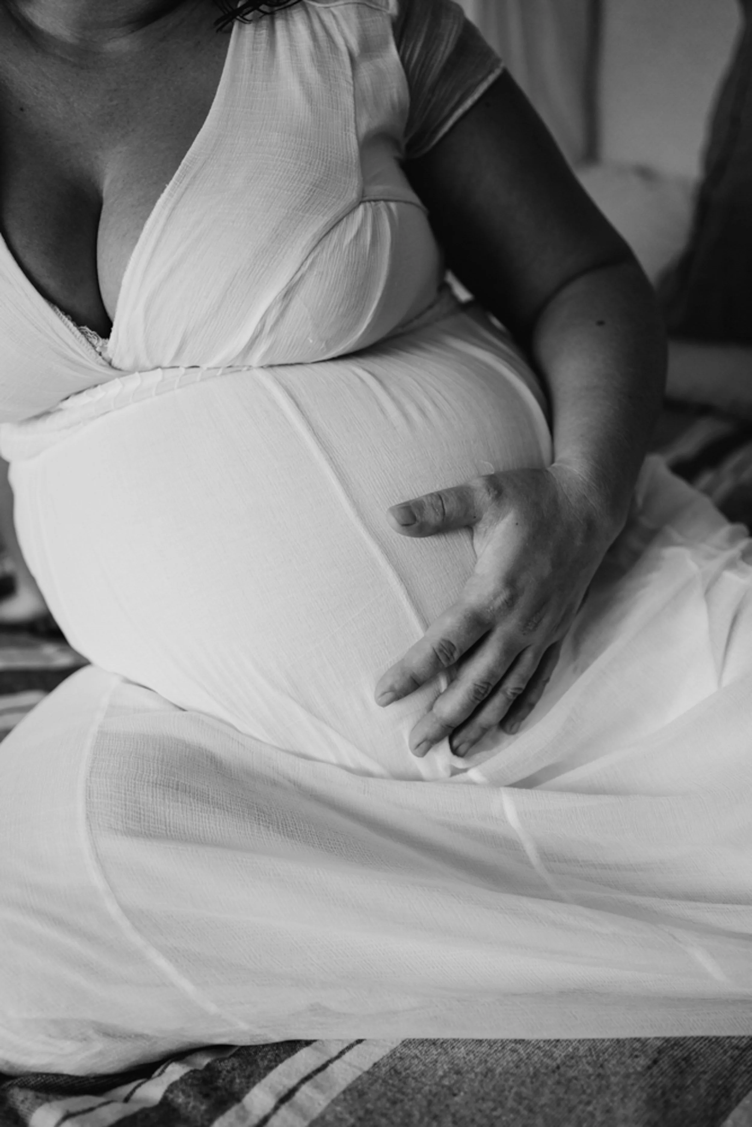 Black and white maternity portrait of pregnant woman gently holding her belly during an intimate motherhood session in Portugal.