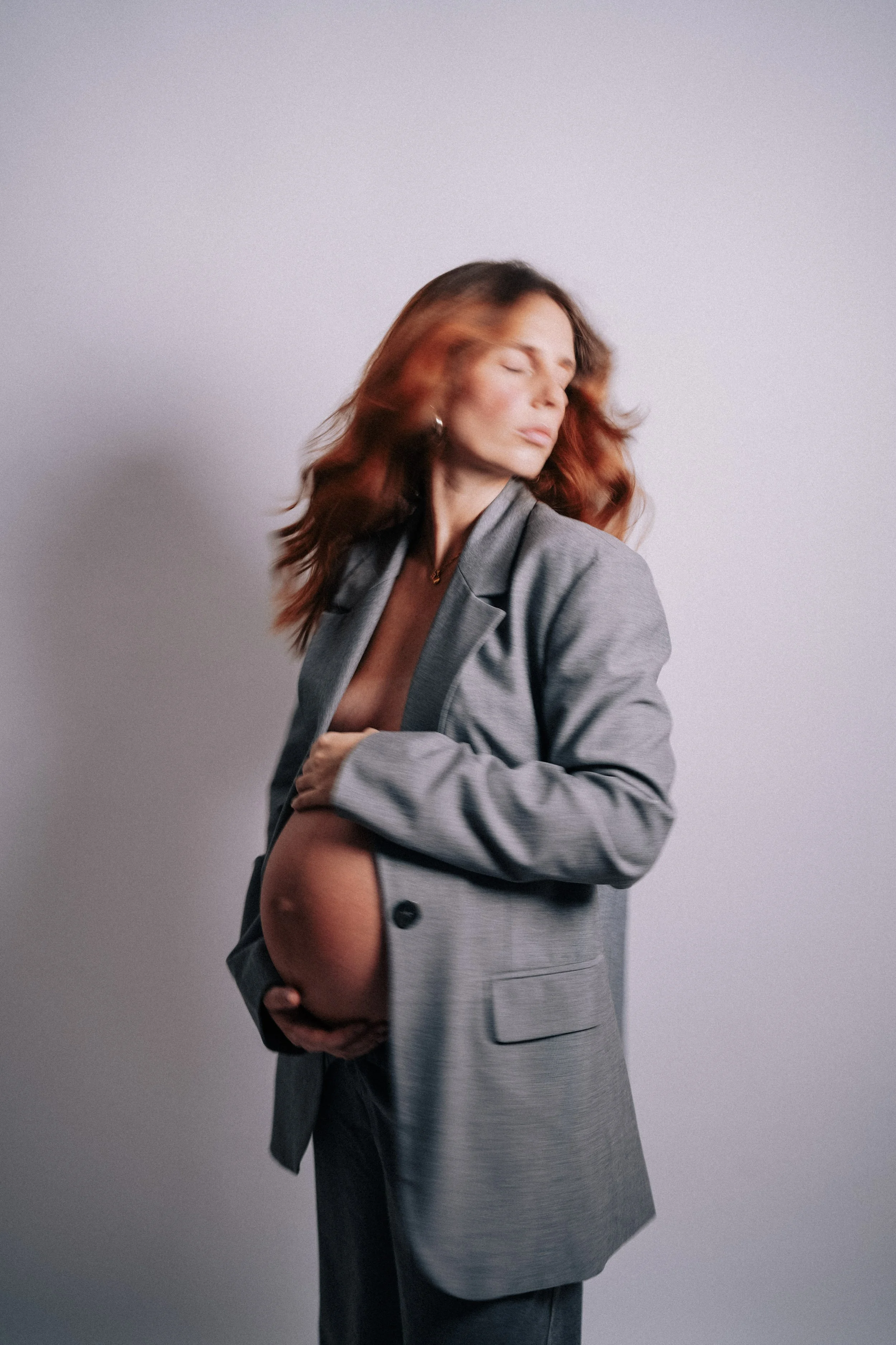 Studio maternity portrait of pregnant woman wearing grey blazer during elegant pregnancy photoshoot in Portugal.