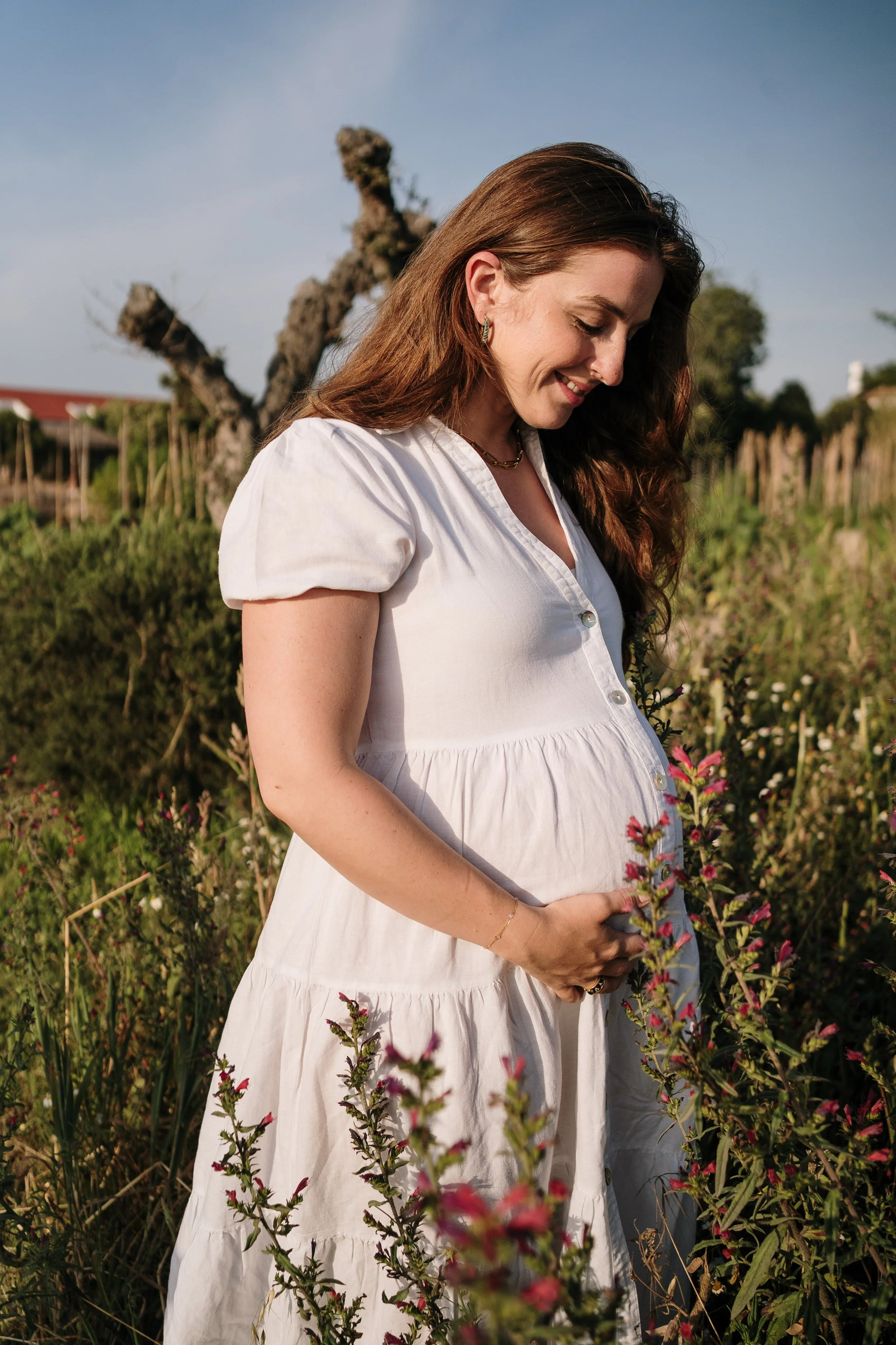 Natural light maternity photoshoot featuring pregnant woman in white dress during outdoor session in Portugal.