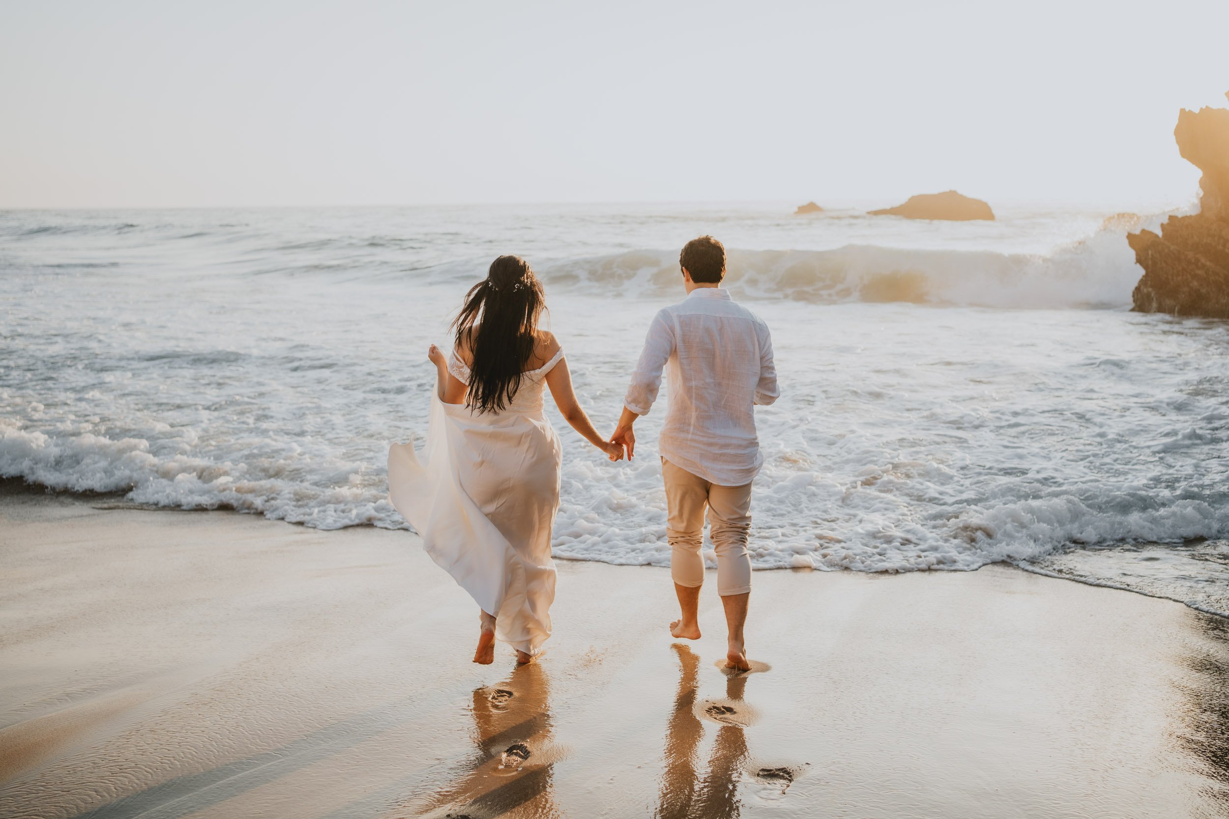 Adventure elopement couple running barefoot on Adraga Beach at sunset in Sintra Portugal