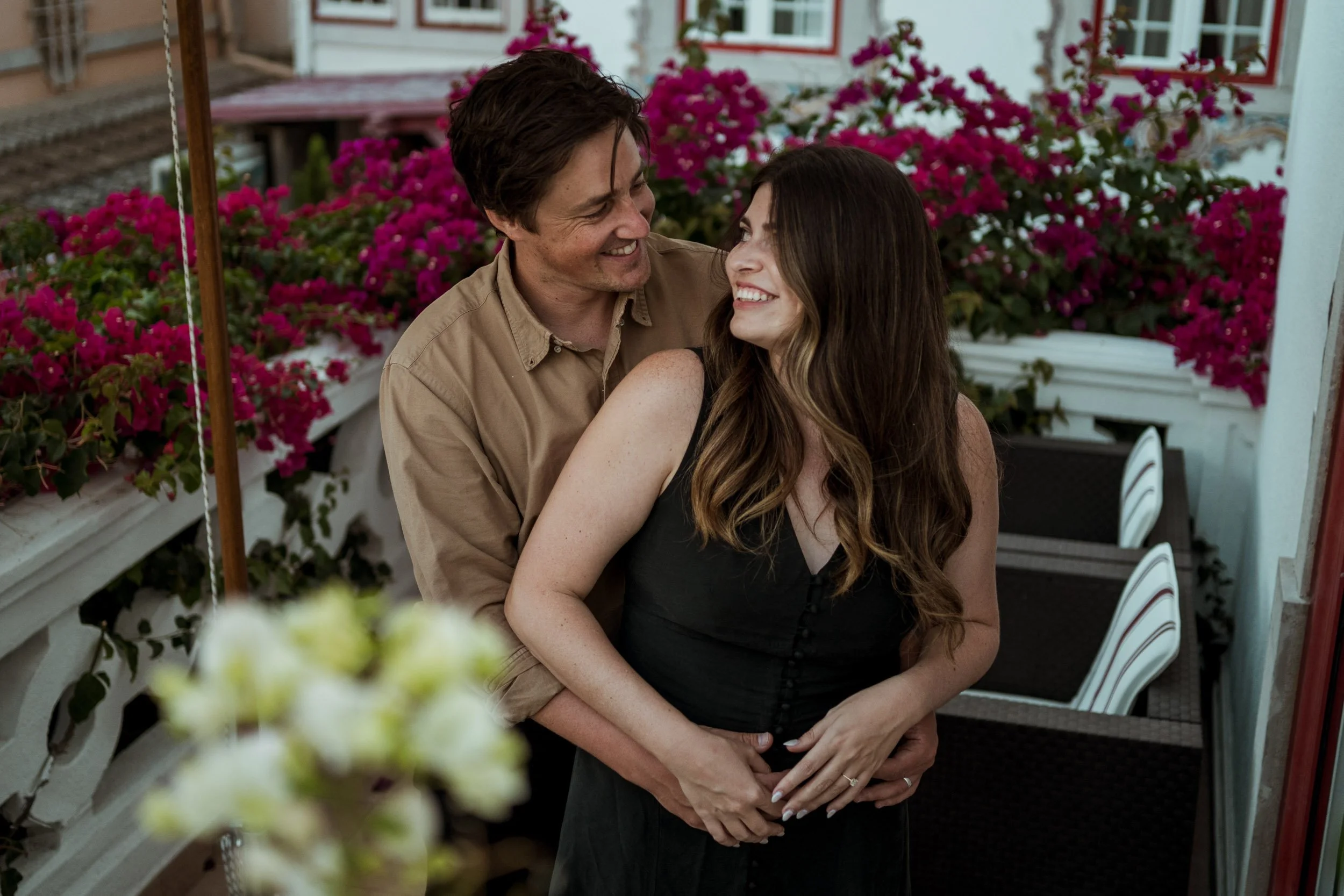 Engagement photography in Lisbon, couple laughing together on balcony surrounded by flowers.