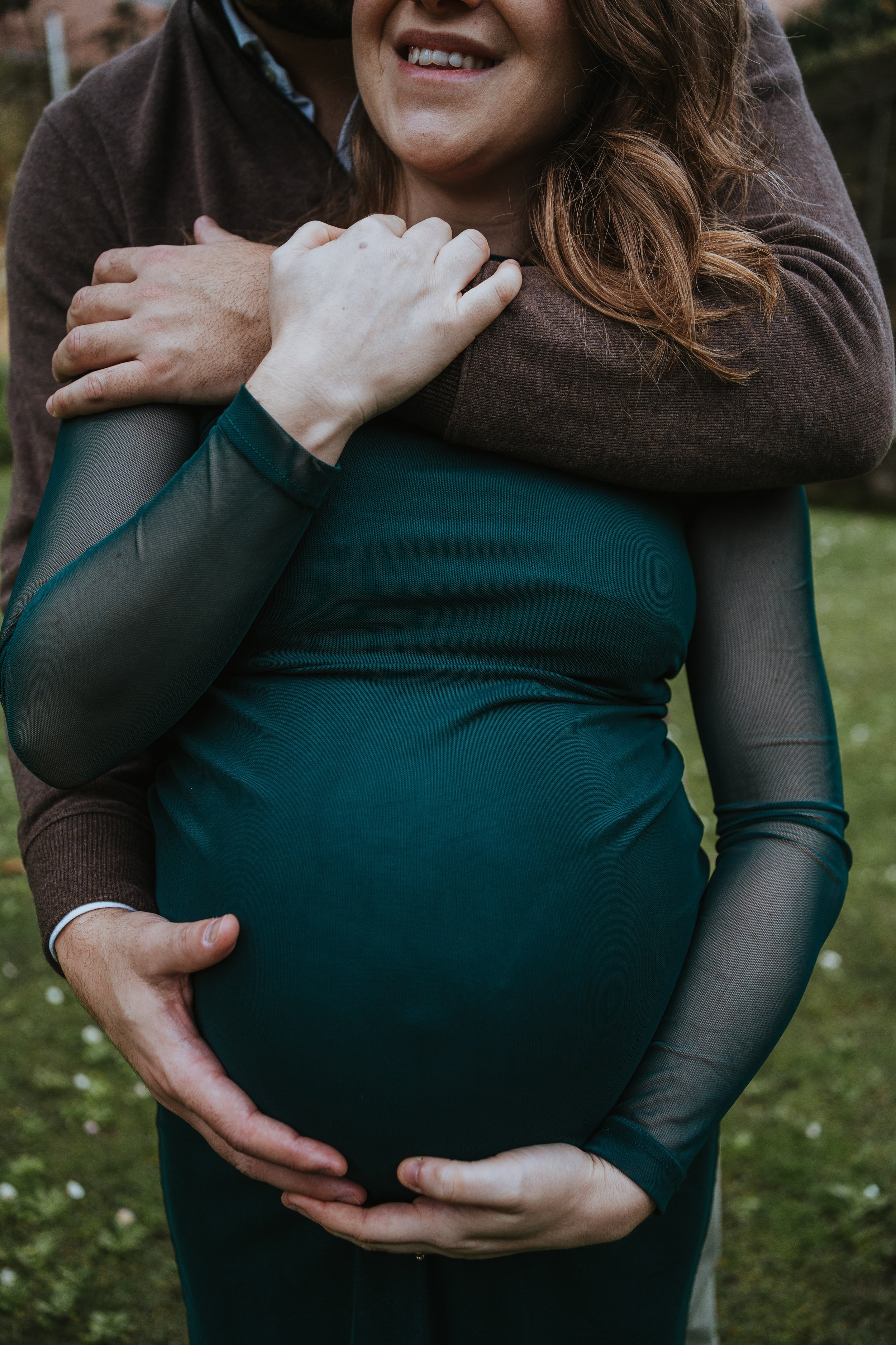 Lifestyle pregnancy photography showing pregnant woman holding her belly during outdoor maternity session.