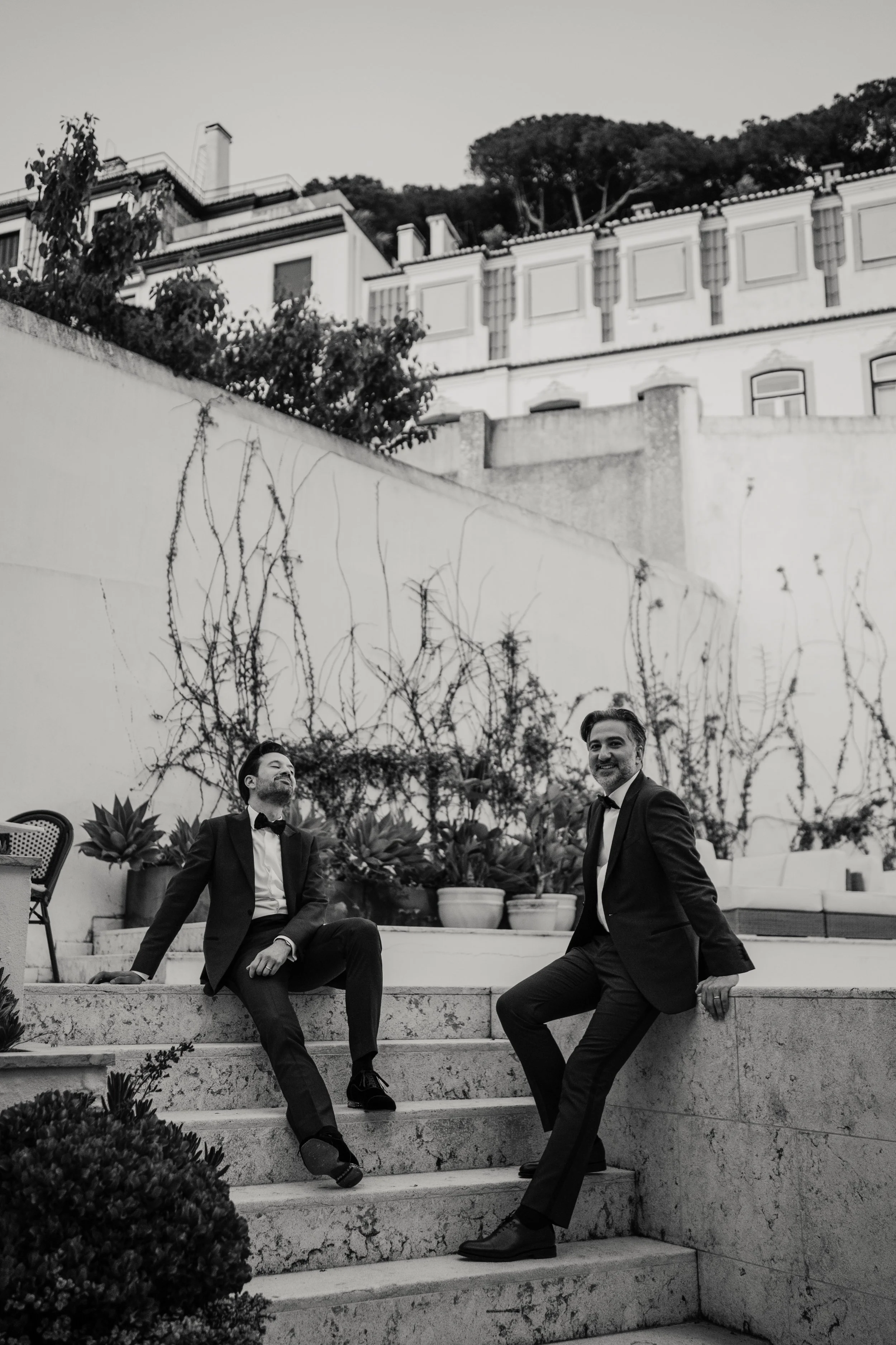 Black and white wedding portrait of alternative couple sitting on stone steps in Portugal