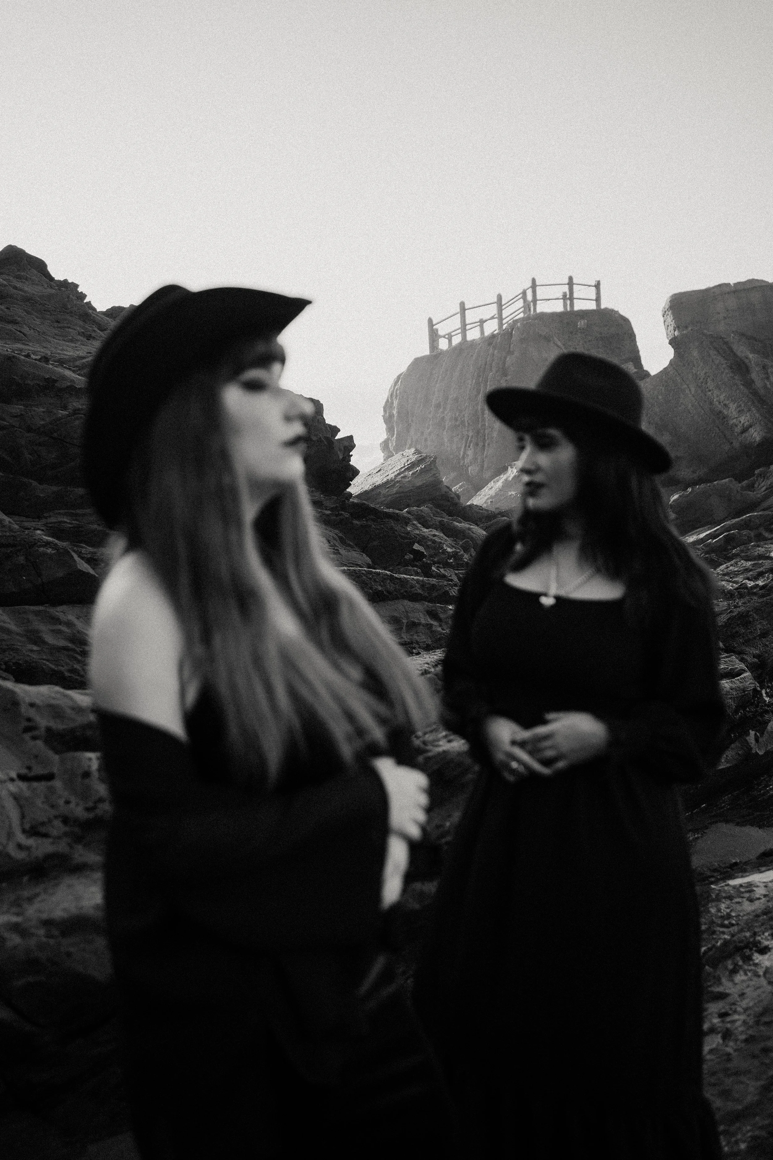 Portugal-based wedding photographers Rose and Elodie from Wandersoul Stories standing on rocky cliffs in cinematic black and white portrait.