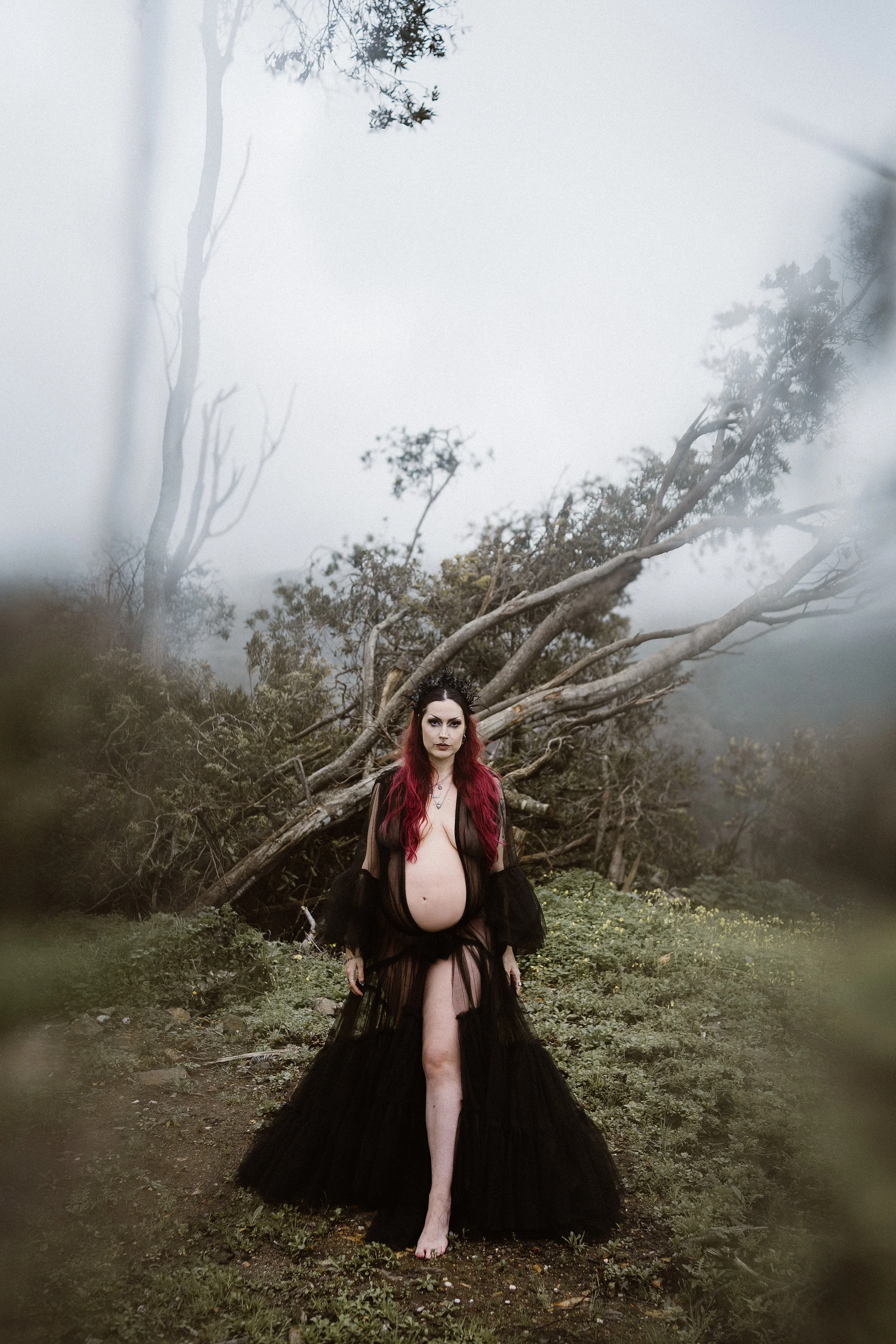 Moody outdoor maternity portrait of pregnant woman standing in misty forest during a motherhood photoshoot in Portugal.