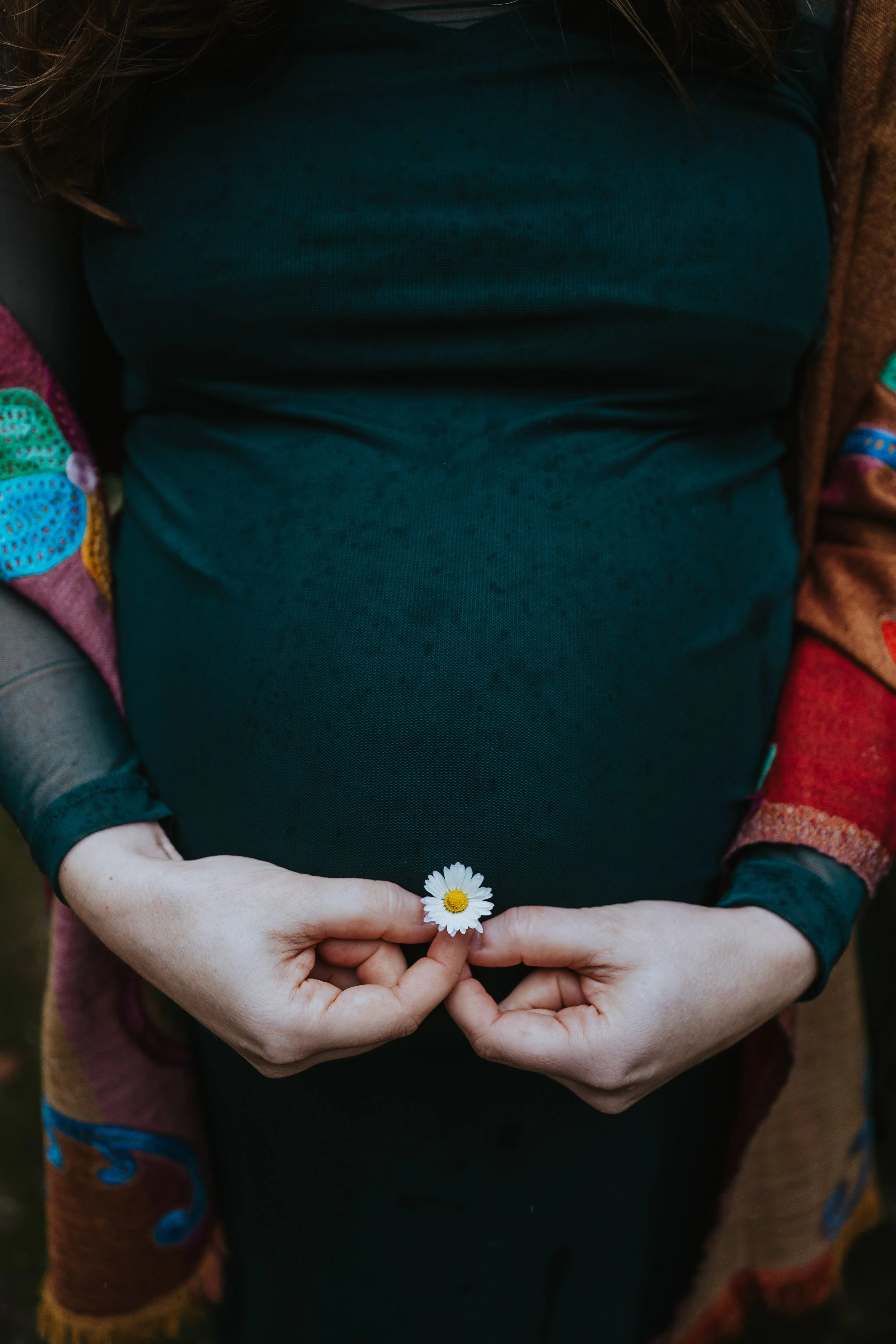 Pregnancy photoshoot detail of hands forming heart shape over baby bump during motherhood session.