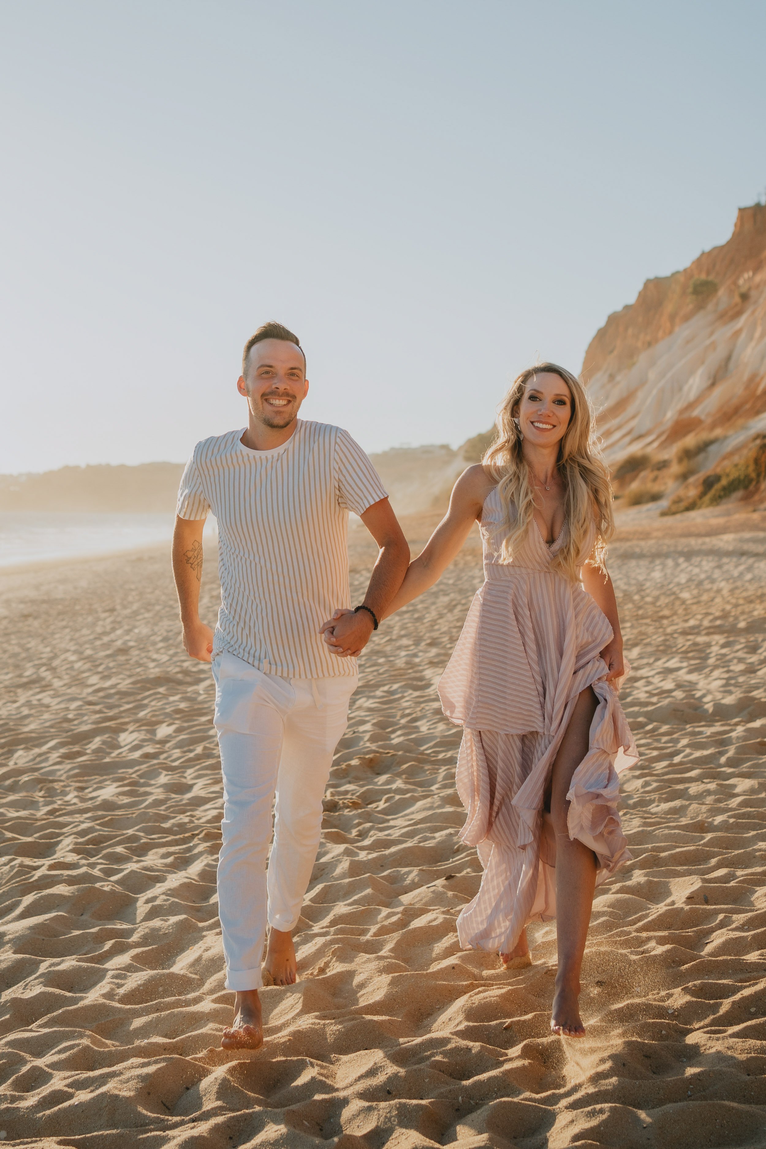 Engagement photography in Algarve, couple running together on sandy beach at sunset.