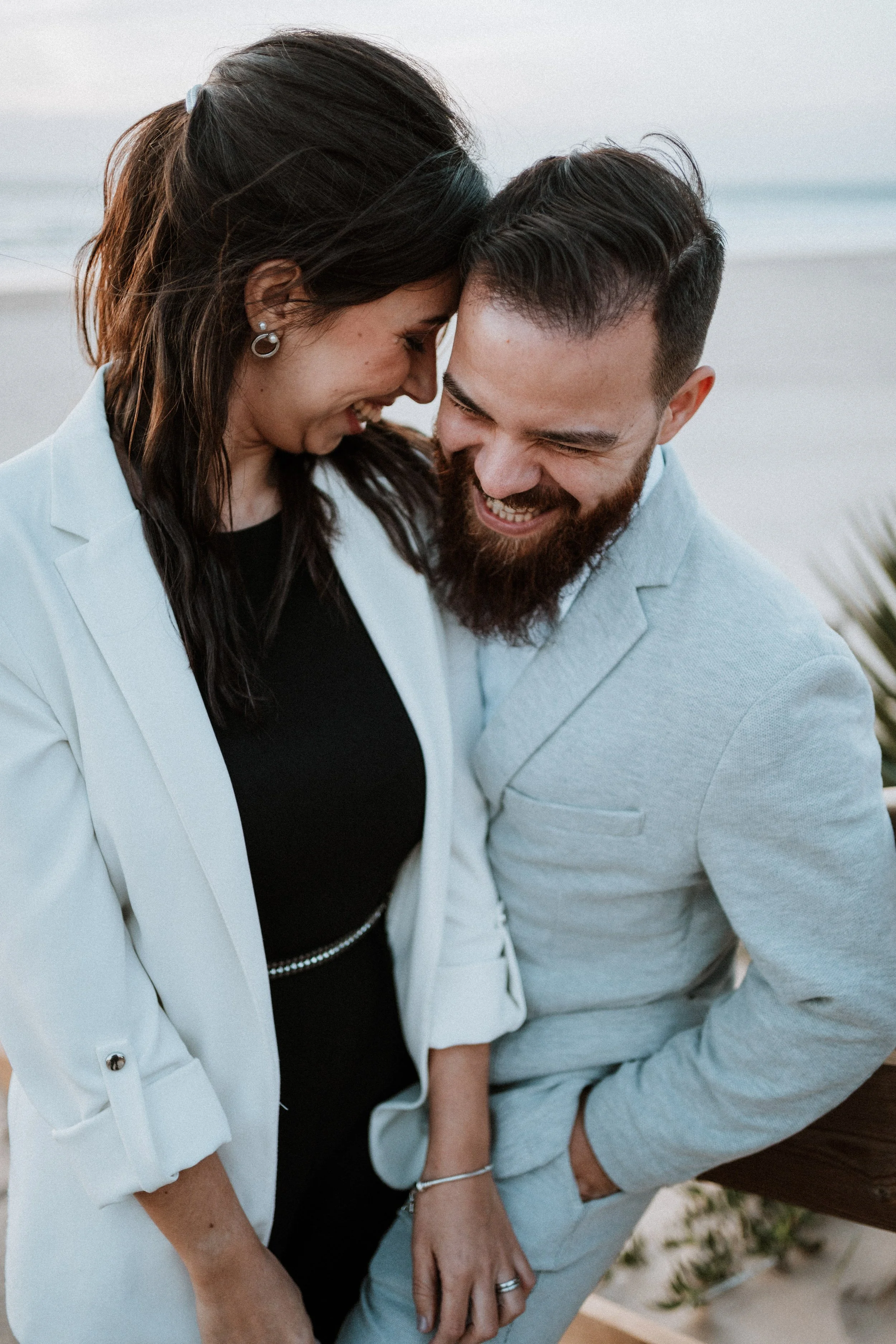 A happy couple sharing a moment at the beach, leaning their foreheads together and smiling.