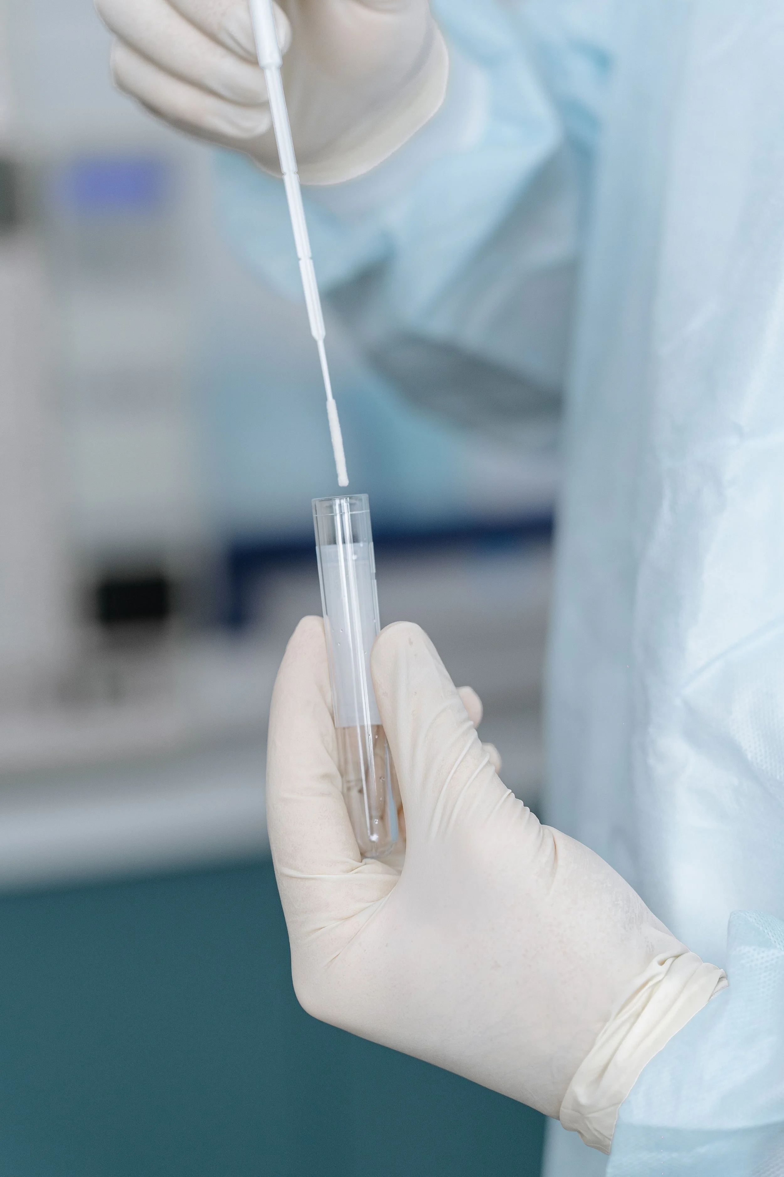 Close-up of a healthcare worker wearing a glove and holding a test tube with a dropper above it, in a laboratory or medical setting.