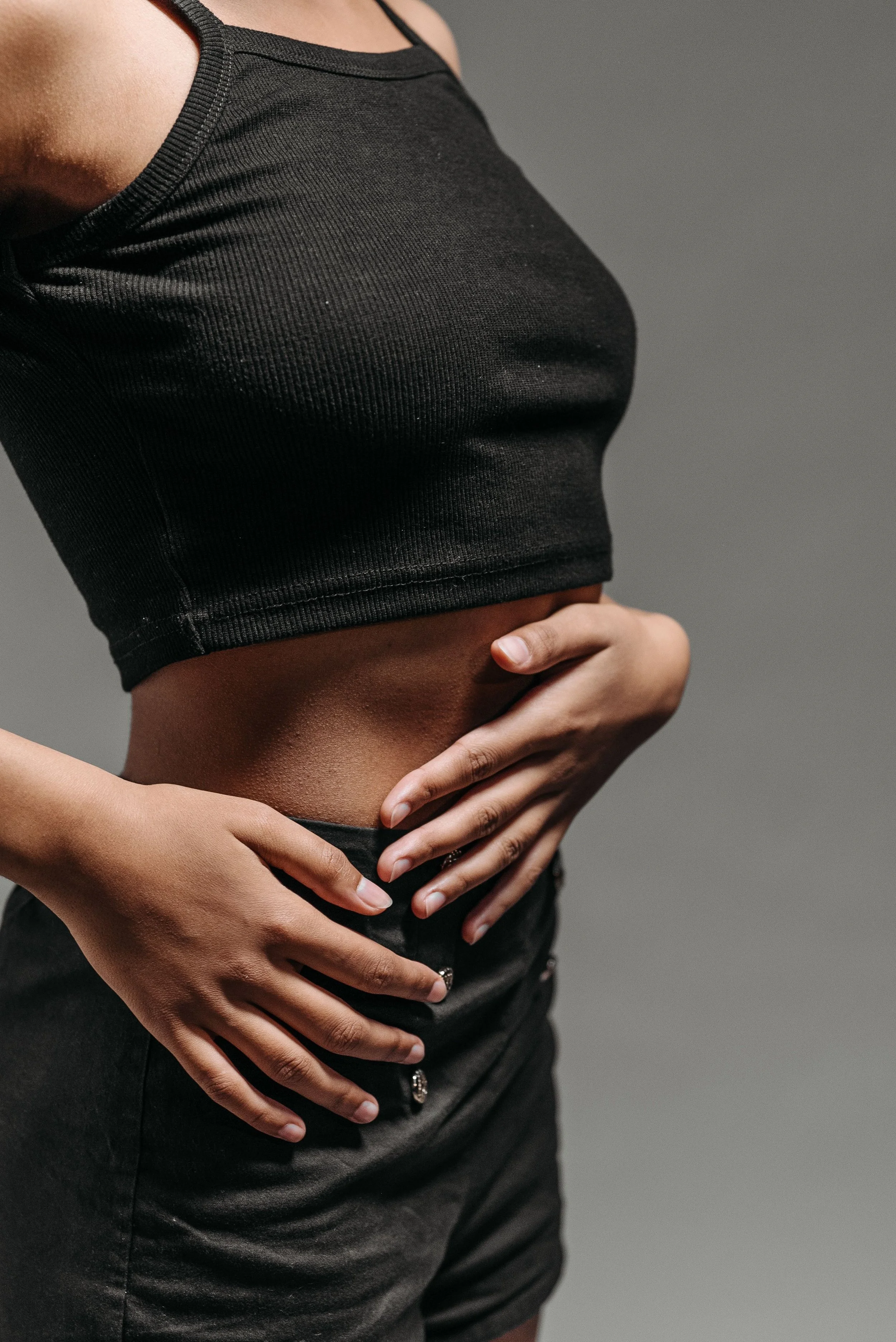 A person wearing a black crop top and black pants with hands on their waist.