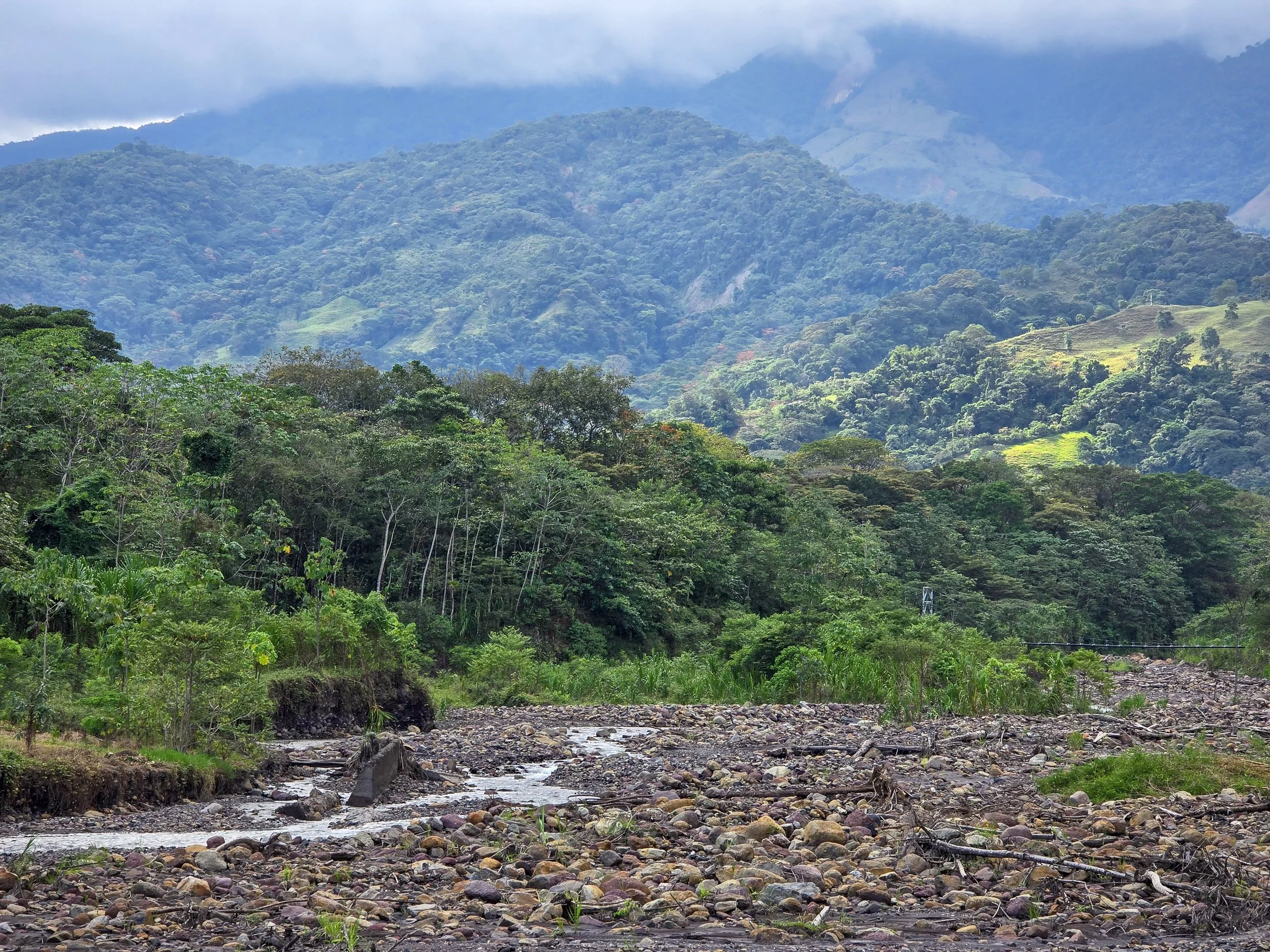 Lush green mountains with a river flowing through a rocky landscape in a tropical rainforest.