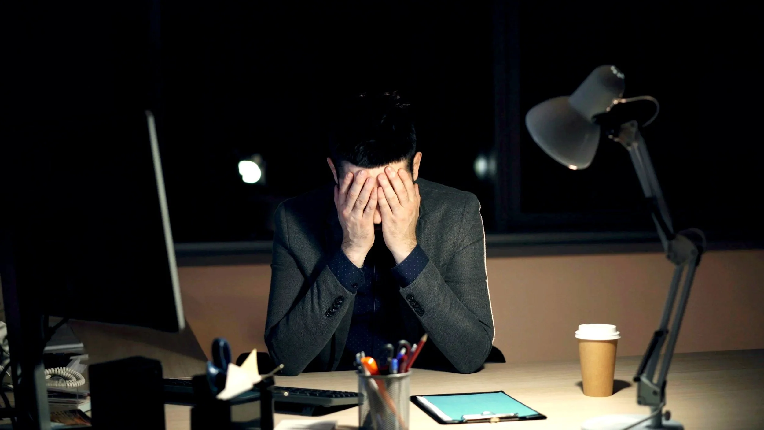 Man in a suit sitting behind a desk with his head in his hands, representing leadership and team performance challenges.