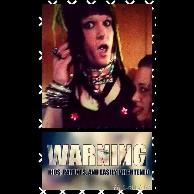 A woman with dark hair and colorful accessories making a surprised or shocked expression, with a young girl partially visible beside her, and a sign below warning about being easily frightened.