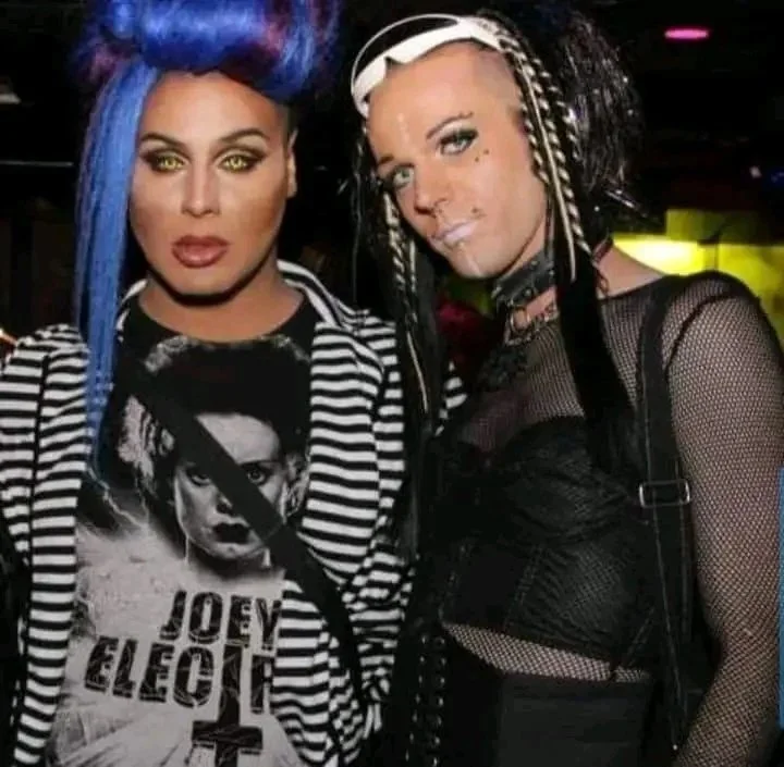 Two women with colorful and edgy hairstyles, wearing alternative fashion, posing together in a nightlife setting.