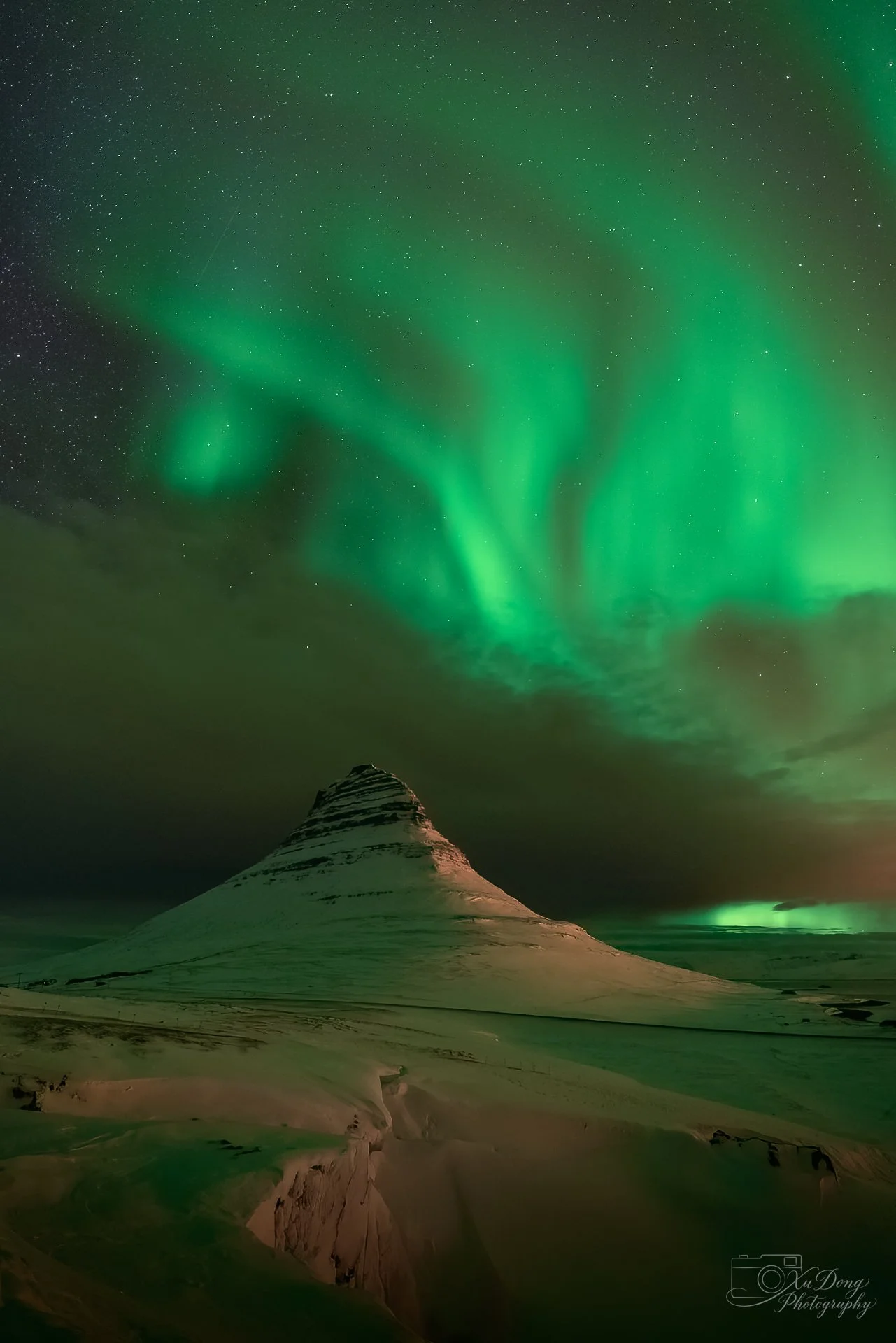 Breathtaking long-exposure photograph of the Aurora Borealis dancing over Kirkjufell mountain in Iceland, capturing the vibrant green Northern Lights against a starlit arctic sky.