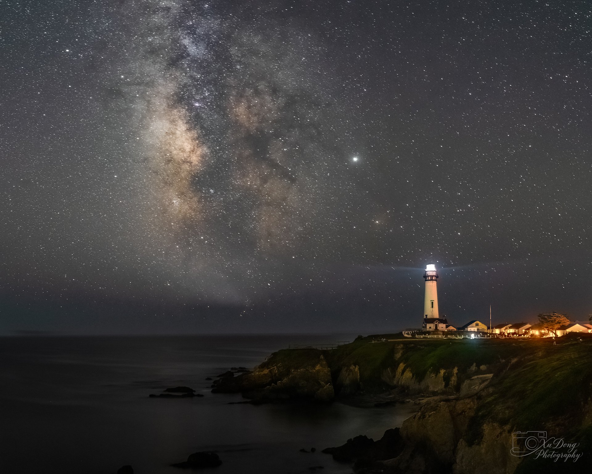 The historic Pigeon Point Lighthouse in California sweeps its beacon across a dark, starry coastal sky, blending maritime history with landscape astrophotography.