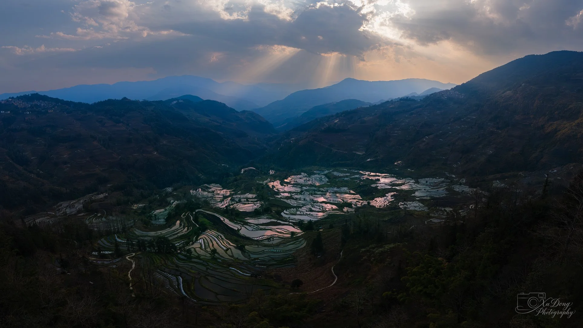 A panoramic golden-hour vista of a quiet Yunnan village valley, where light dances across the rolling landscape