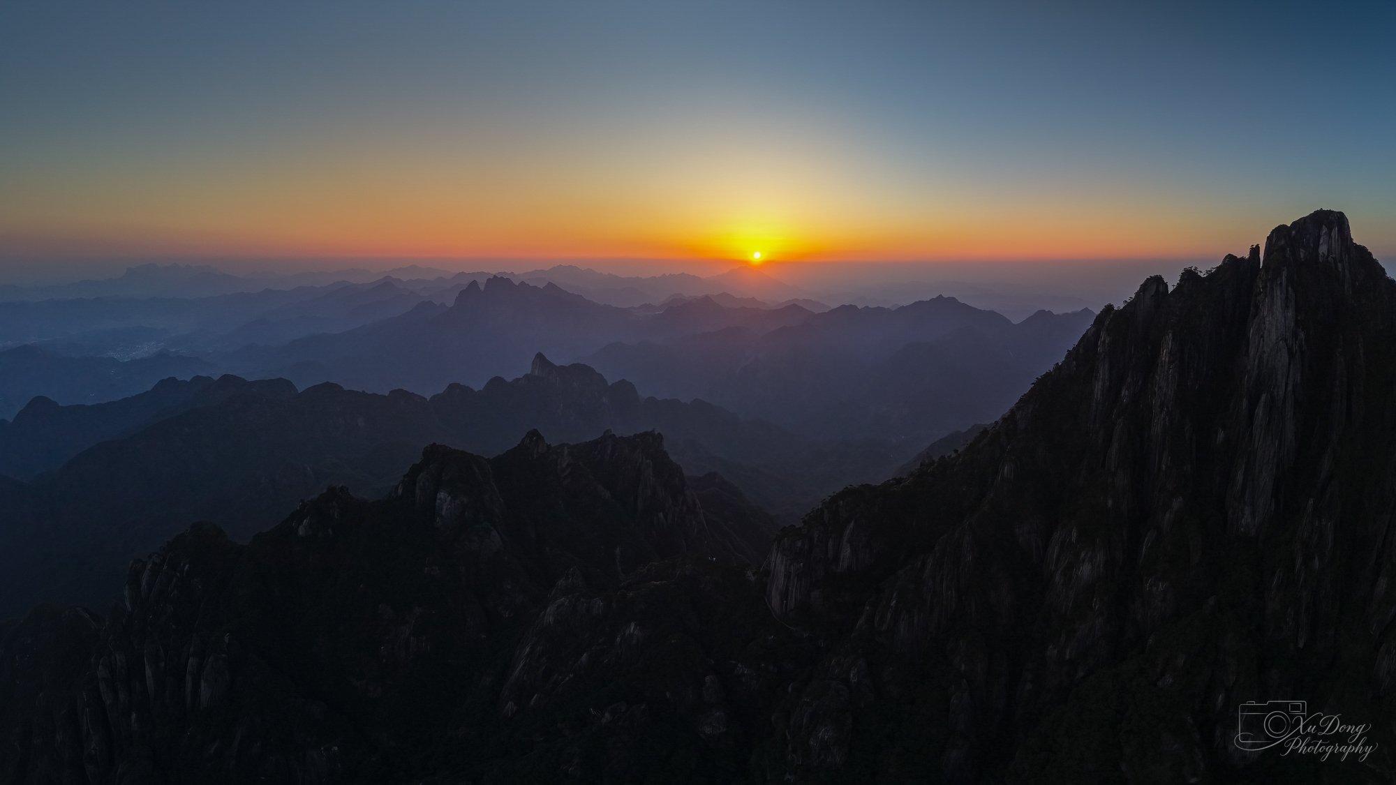 A wide-angle panorama of the Huangshan "Sea of Clouds," where jagged mountain peaks pierce through a soft, white blanket.