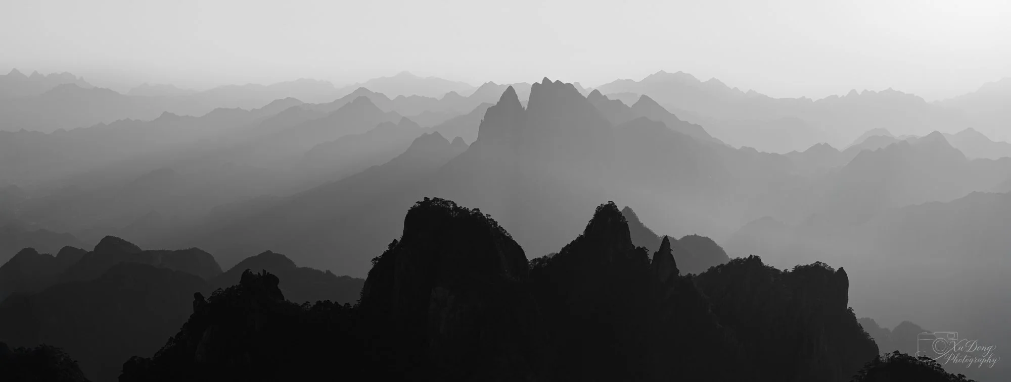 Ethereal fine art photography of mountain peaks disappearing into thick white clouds and mist.