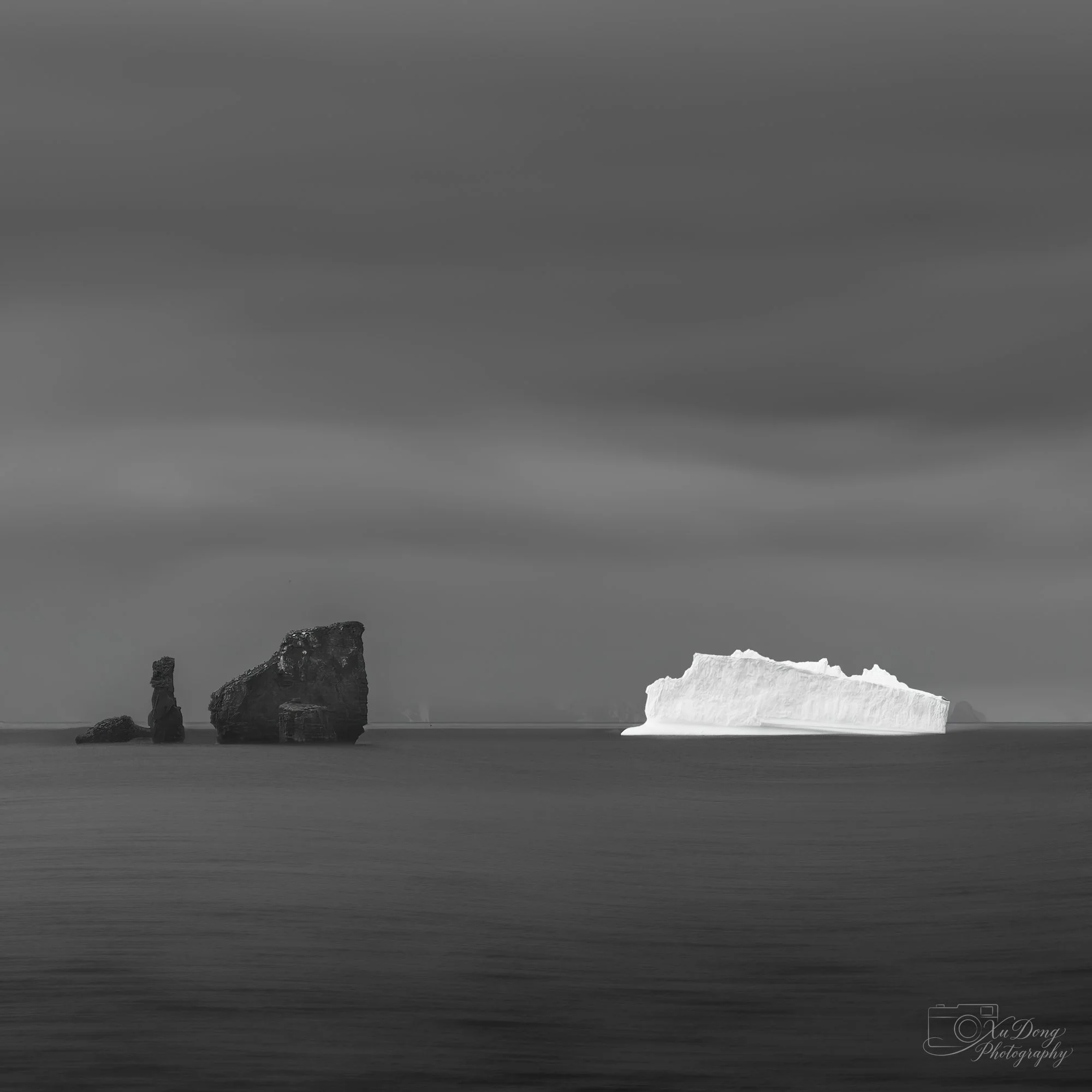 Monochrome fine art photography of a majestic iceberg floating in dark, still polar waters
