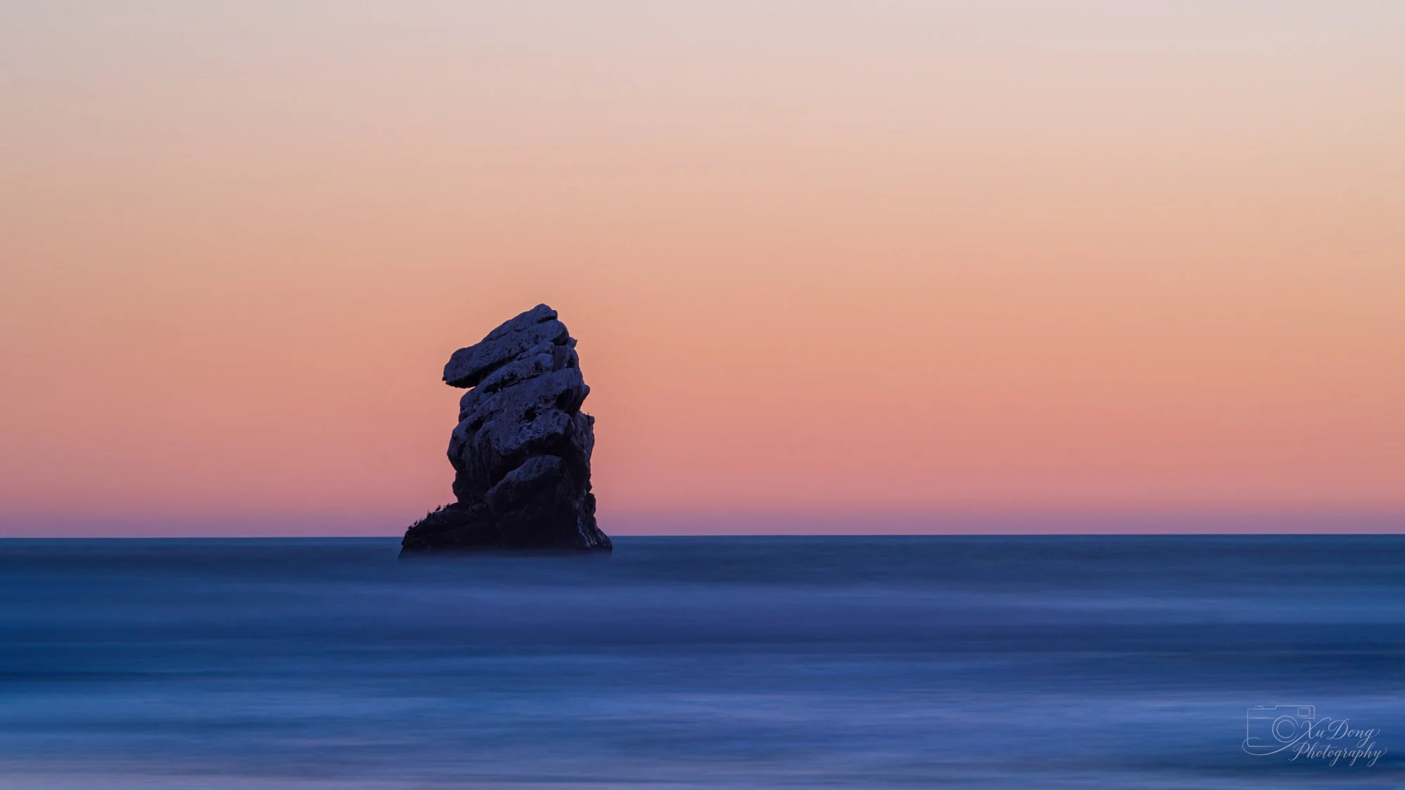 Minimalist long exposure photography of a solitary sea stack rising from the ocean at twilight