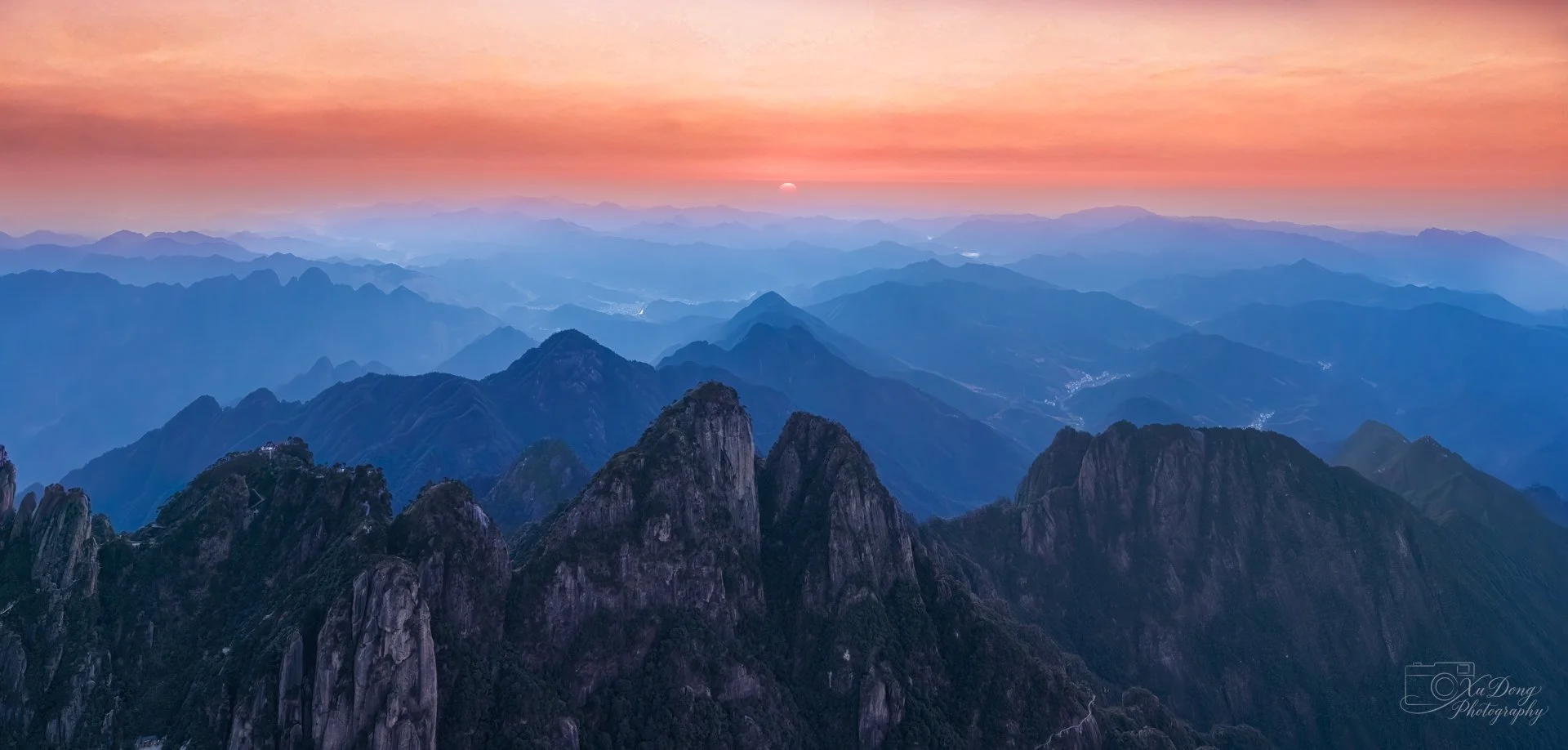 Panoramic sunrise view over a jagged mountain range with orange and blue atmospheric layers