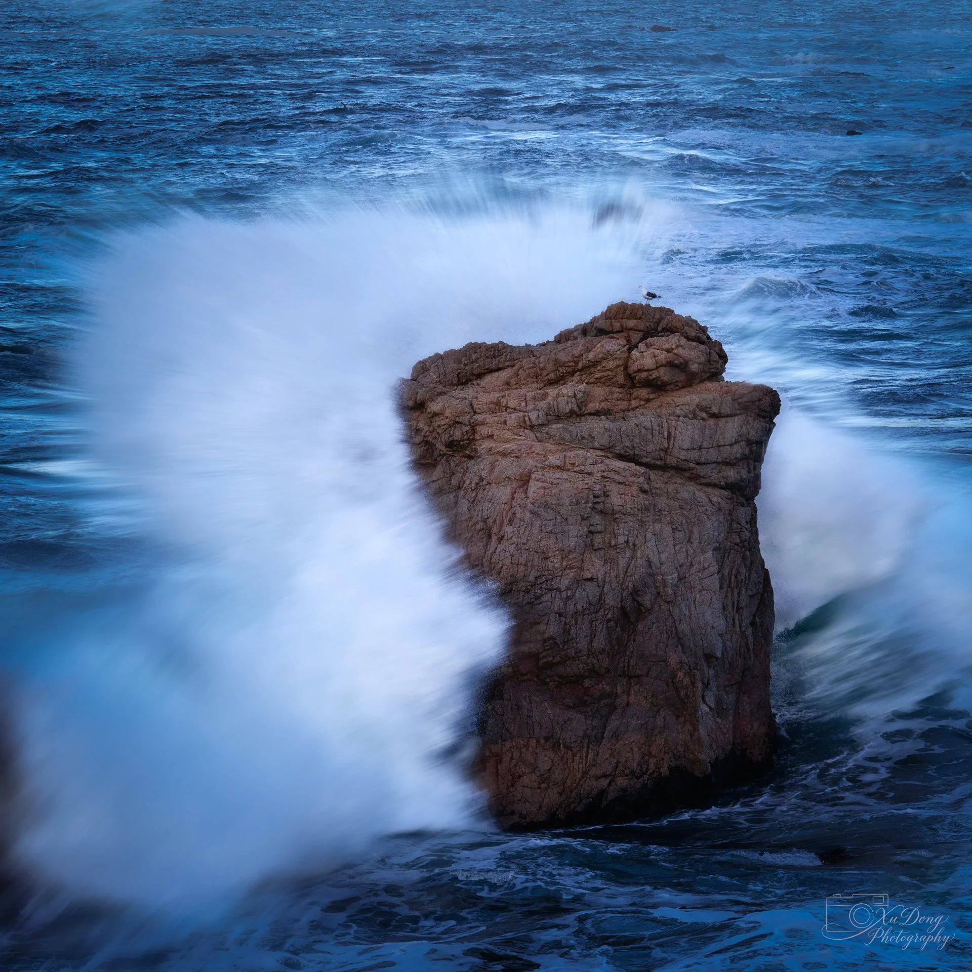 Dramatic fine art photograp[hy of large, powerful ocean waves crashing against jagged coastal rocks