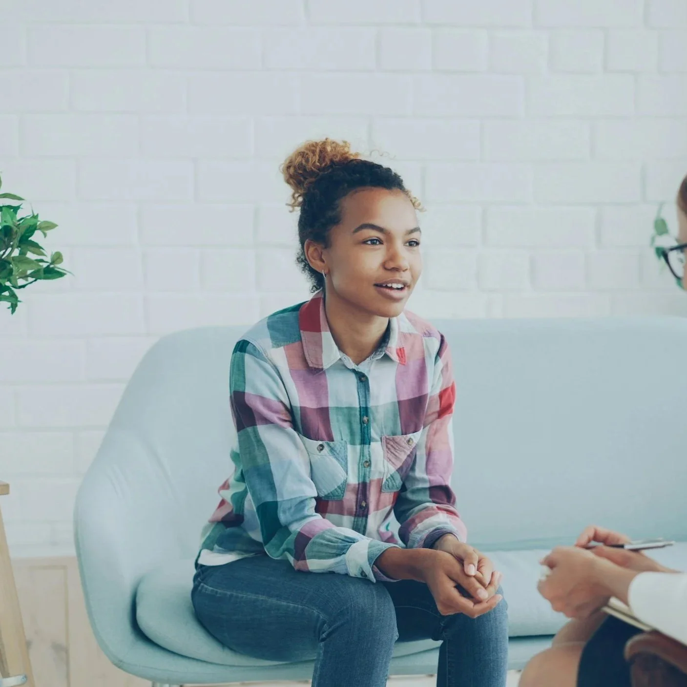 A stock photo of a teenager sitting on a couch in an individual therapy session