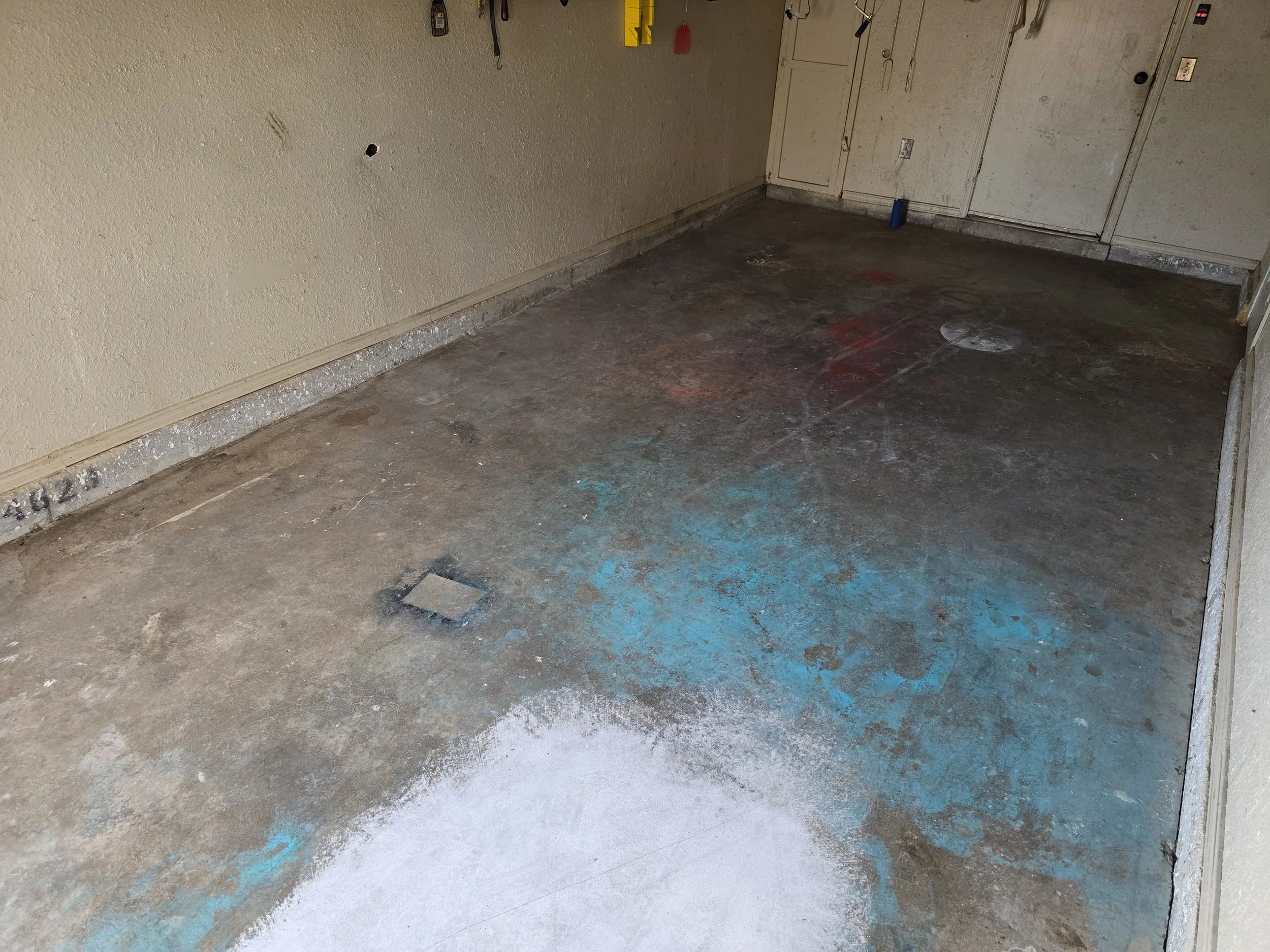 The starting point — a heavily abused garage floor showing years of staining, paint, and neglect. Surface prep begins here.