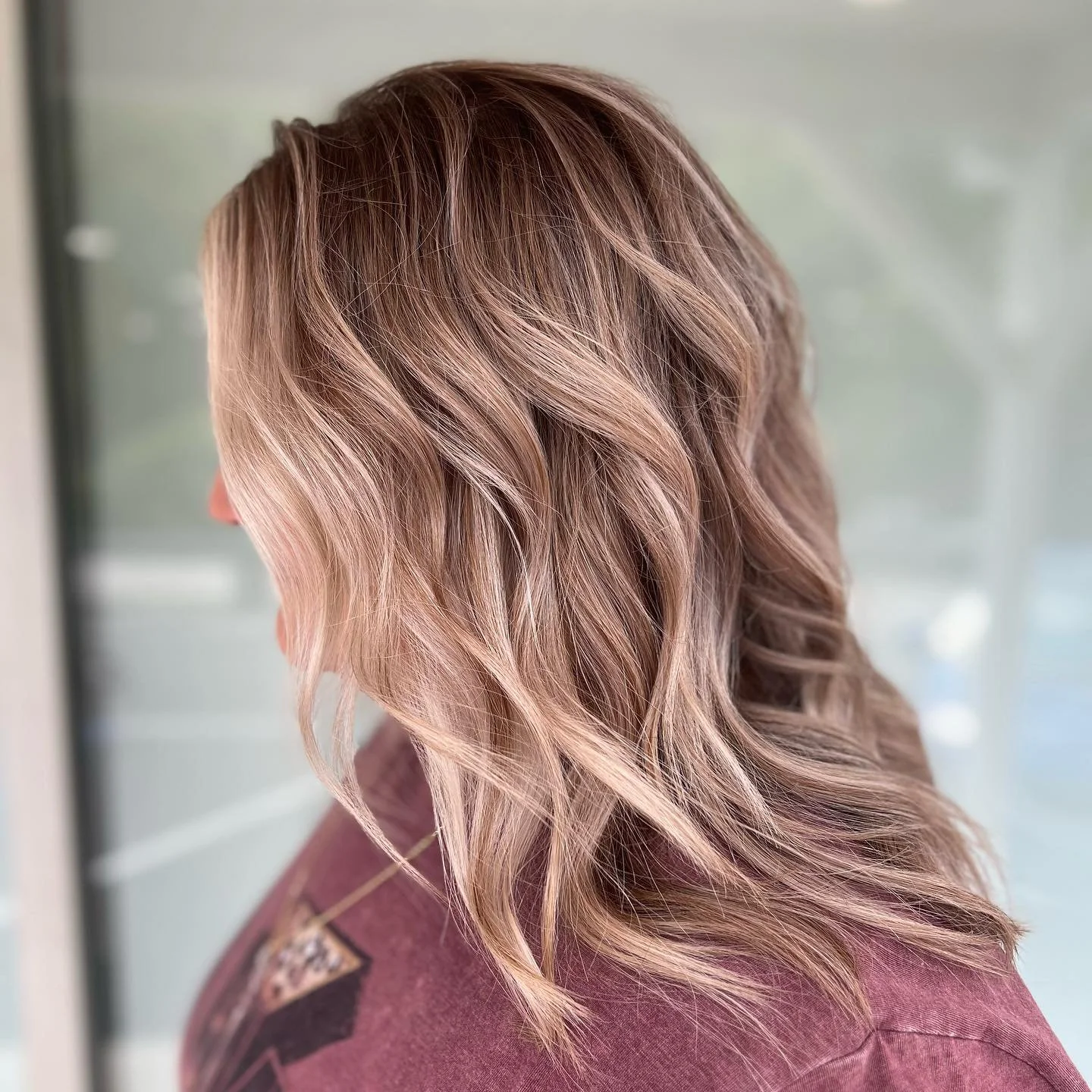 Close-up of a woman's shoulder-length wavy hair with blonde highlights, wearing a maroon top.