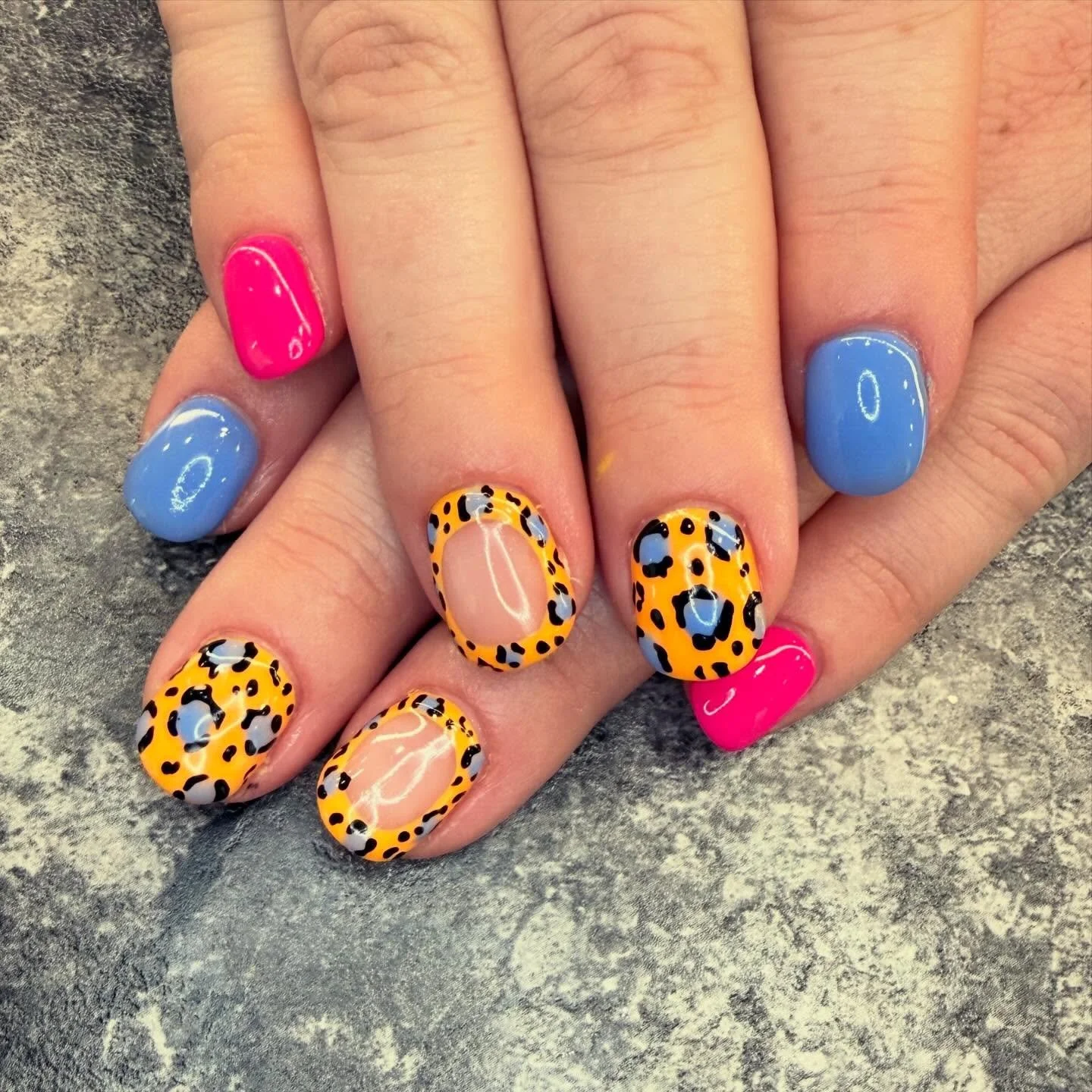 Manicured fingernails with bright pink, blue, and leopard print nail polish.