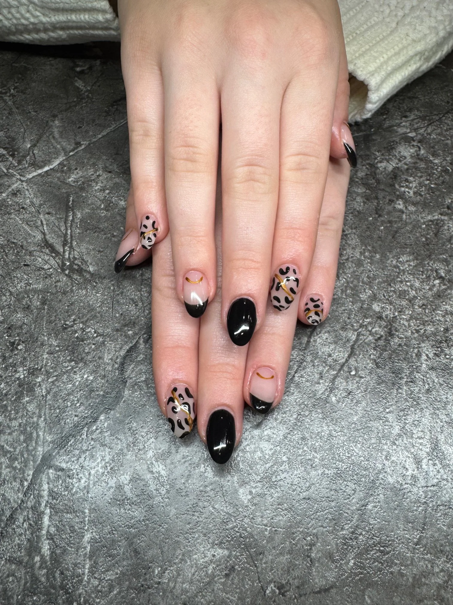 A hand with leopard print and black French tip nail designs resting on a textured gray surface.